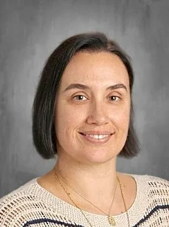 Portrait of a woman with dark hair in a bob style, wearing a striped shirt, smiling lightly, against a gray background.