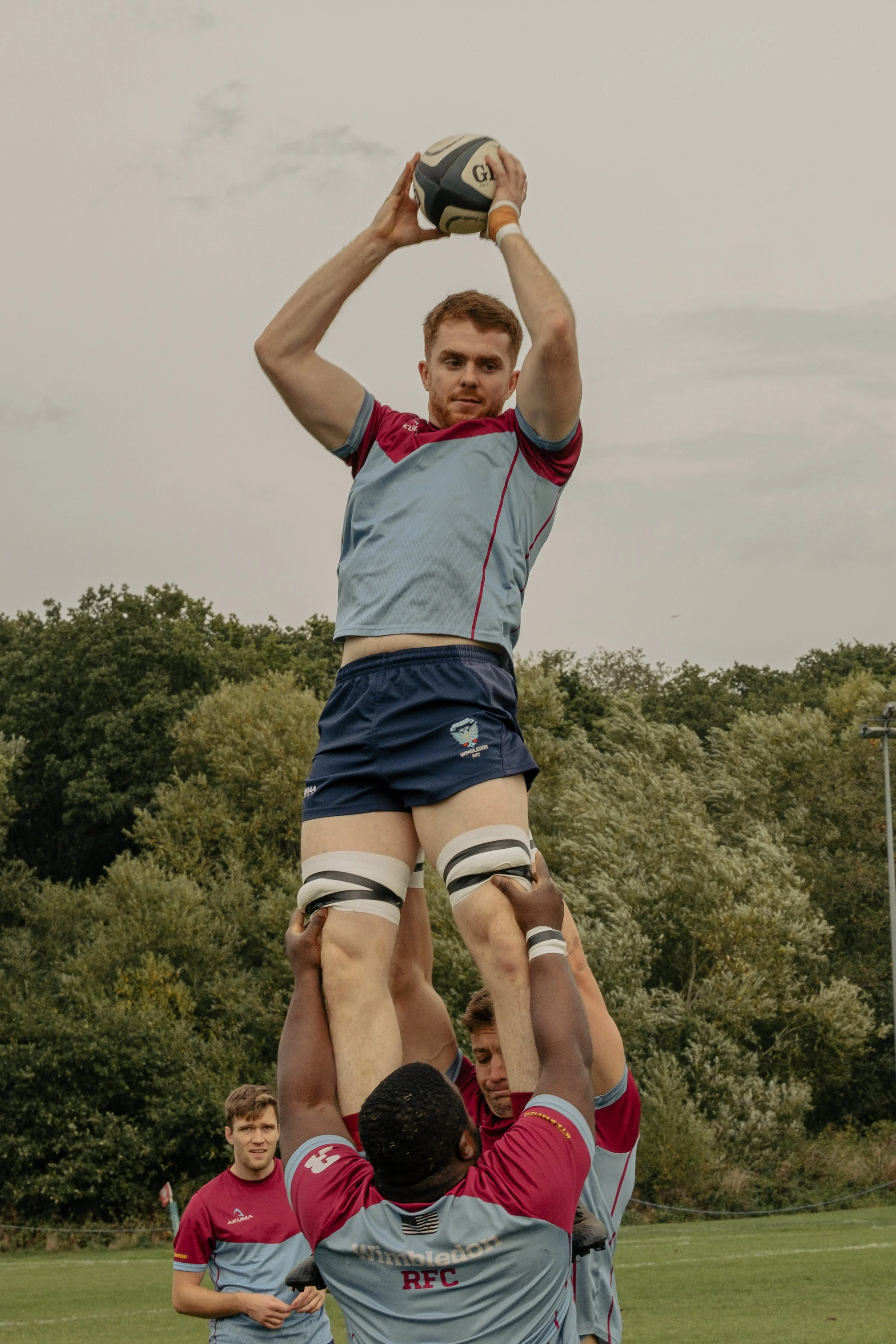Rugby players performing a line-out practice on the field with rugby goals in the background.