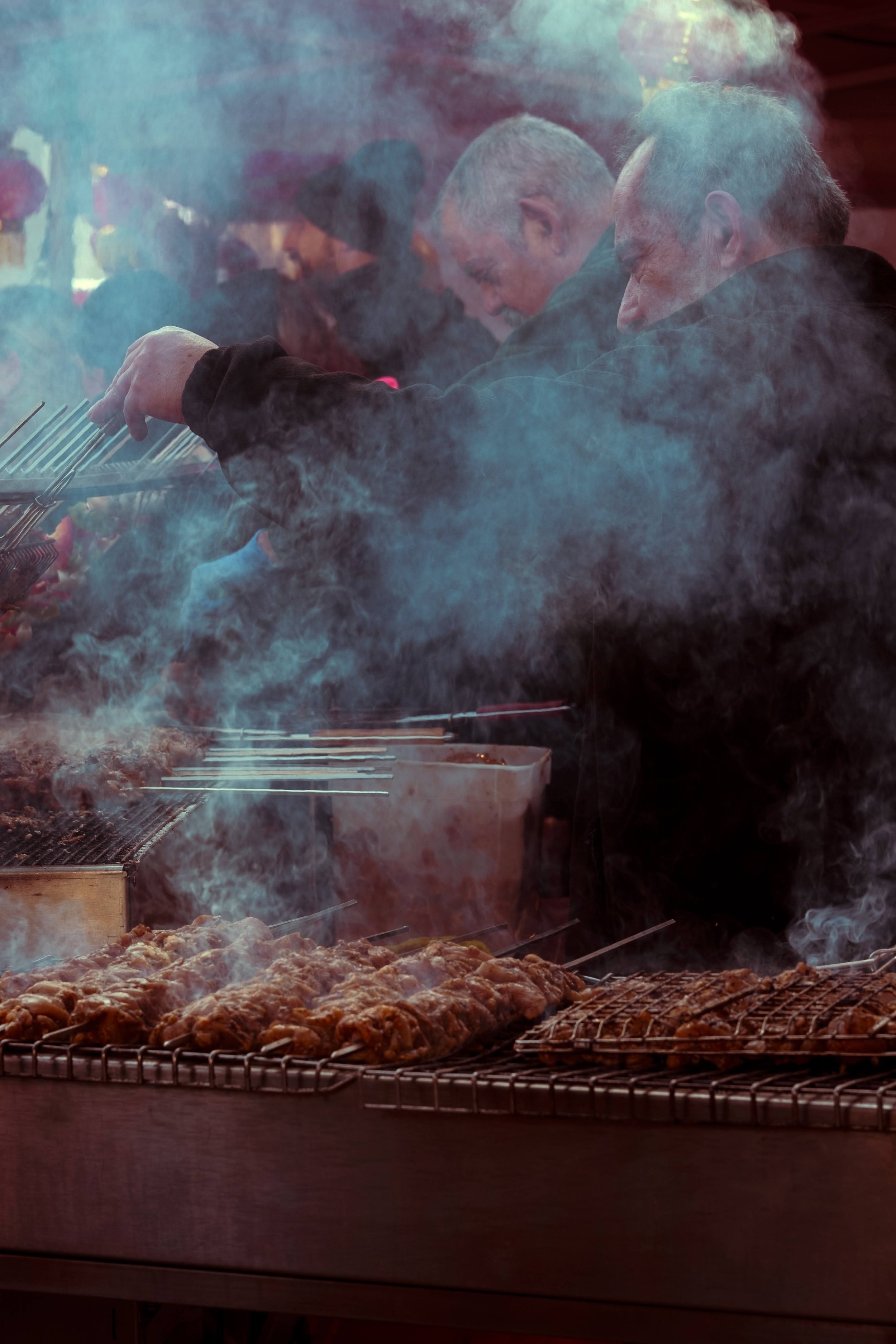 People grilling food at a barbecue with smoke rising around them.