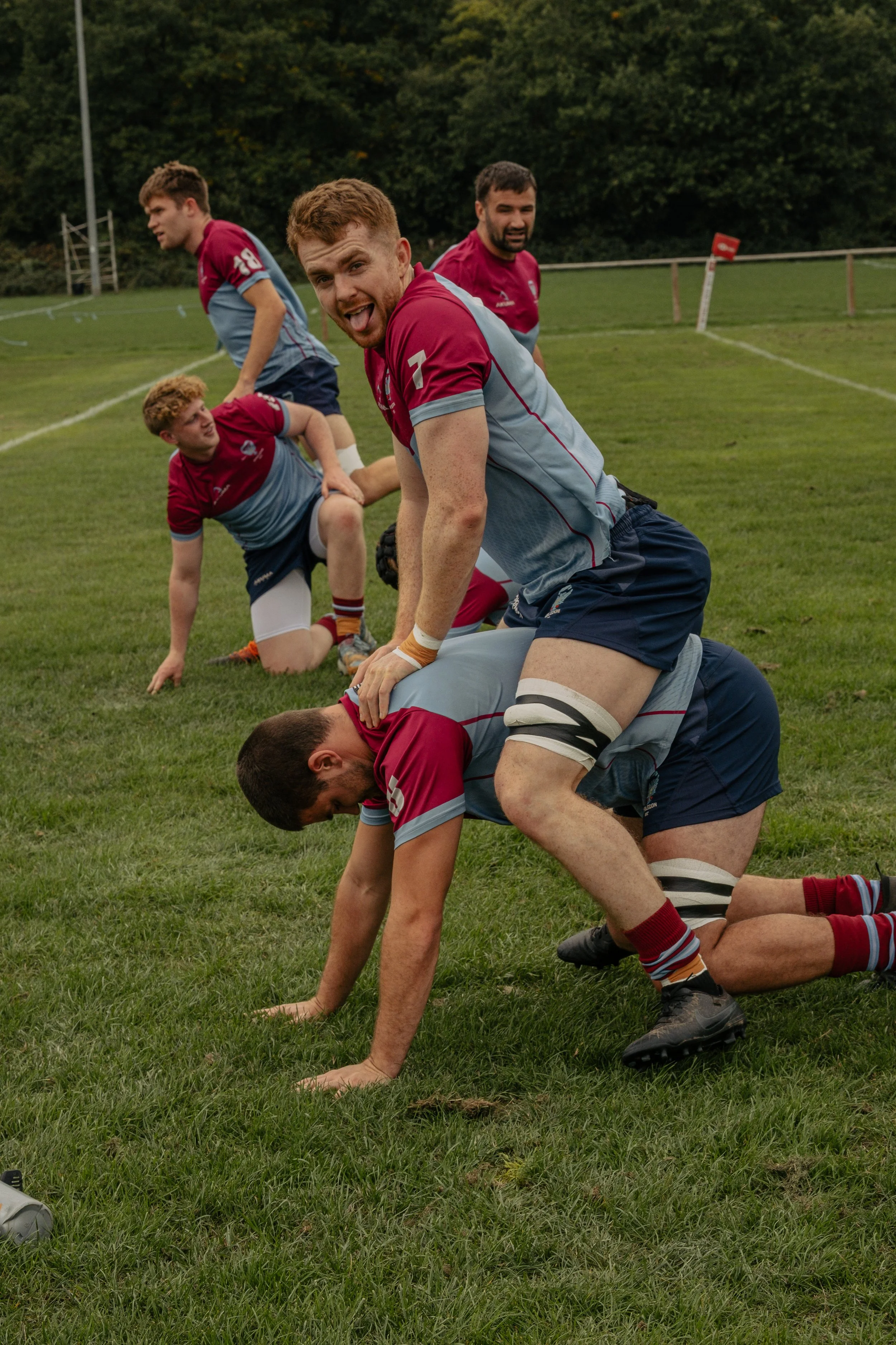 Rugby players practicing scrum on the field with one player smiling at camera.