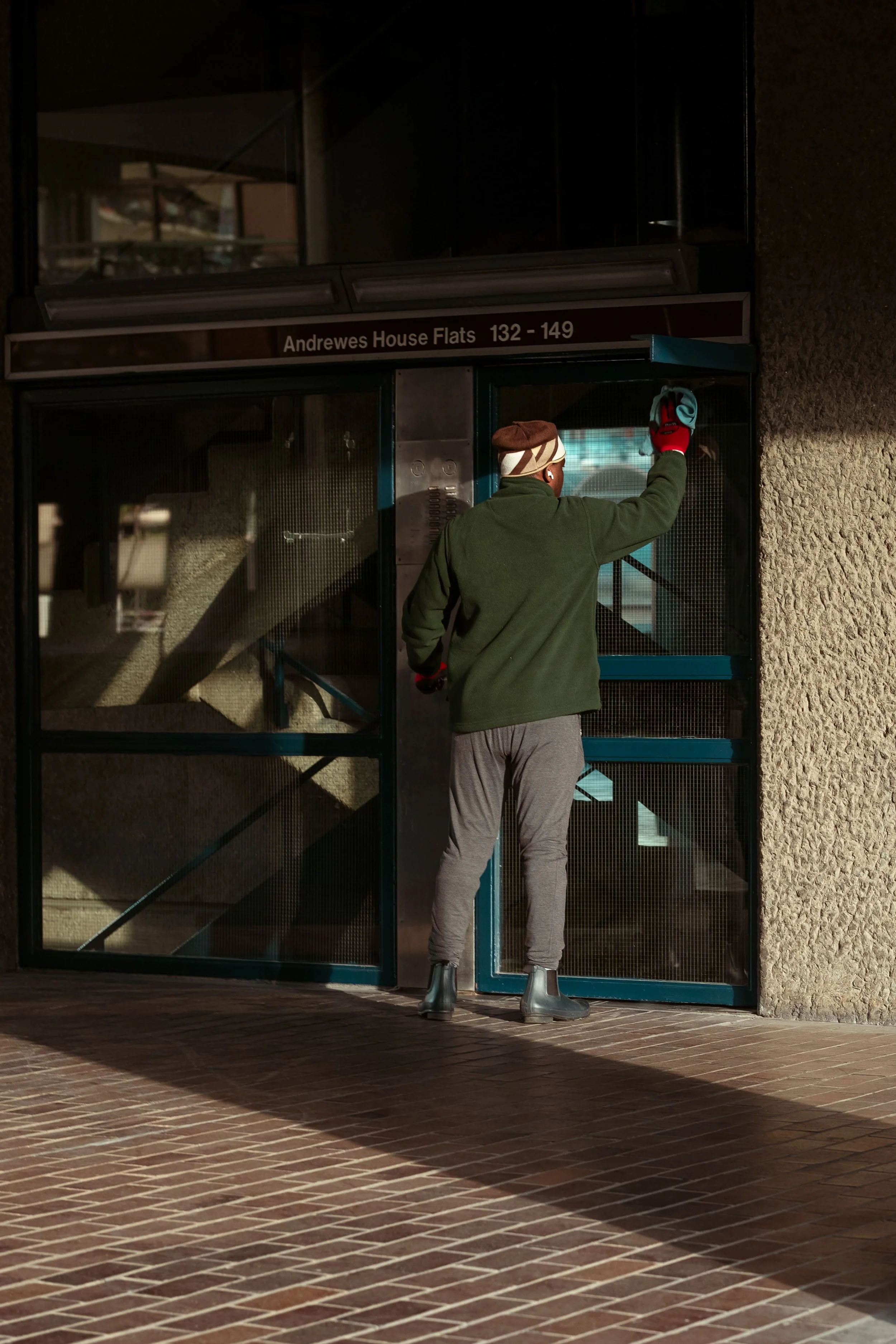 A person standing outside a building wiping the glass door with a cloth.