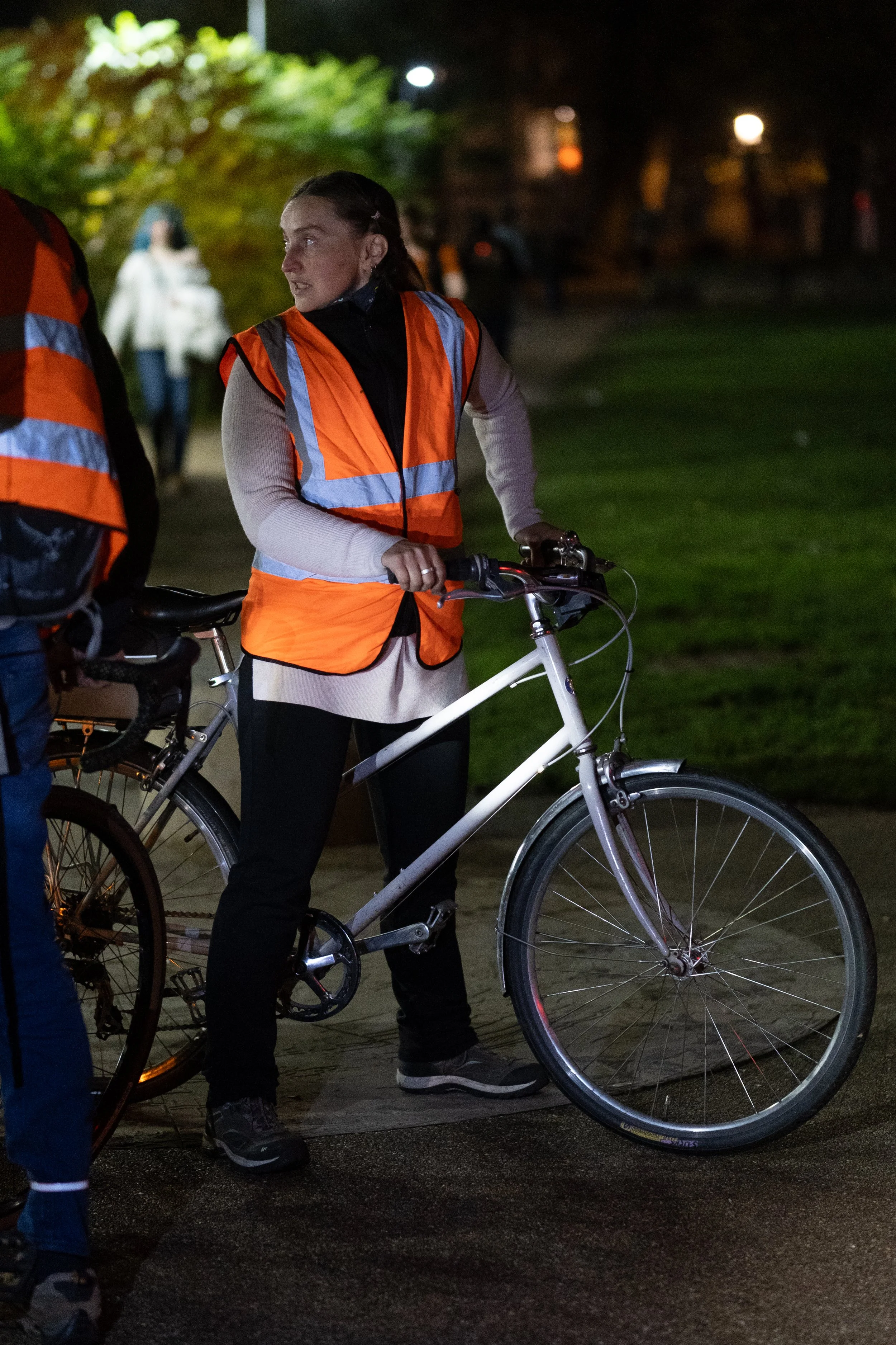 A woman in an orange reflective safety vest standing next to a bicycle at night.