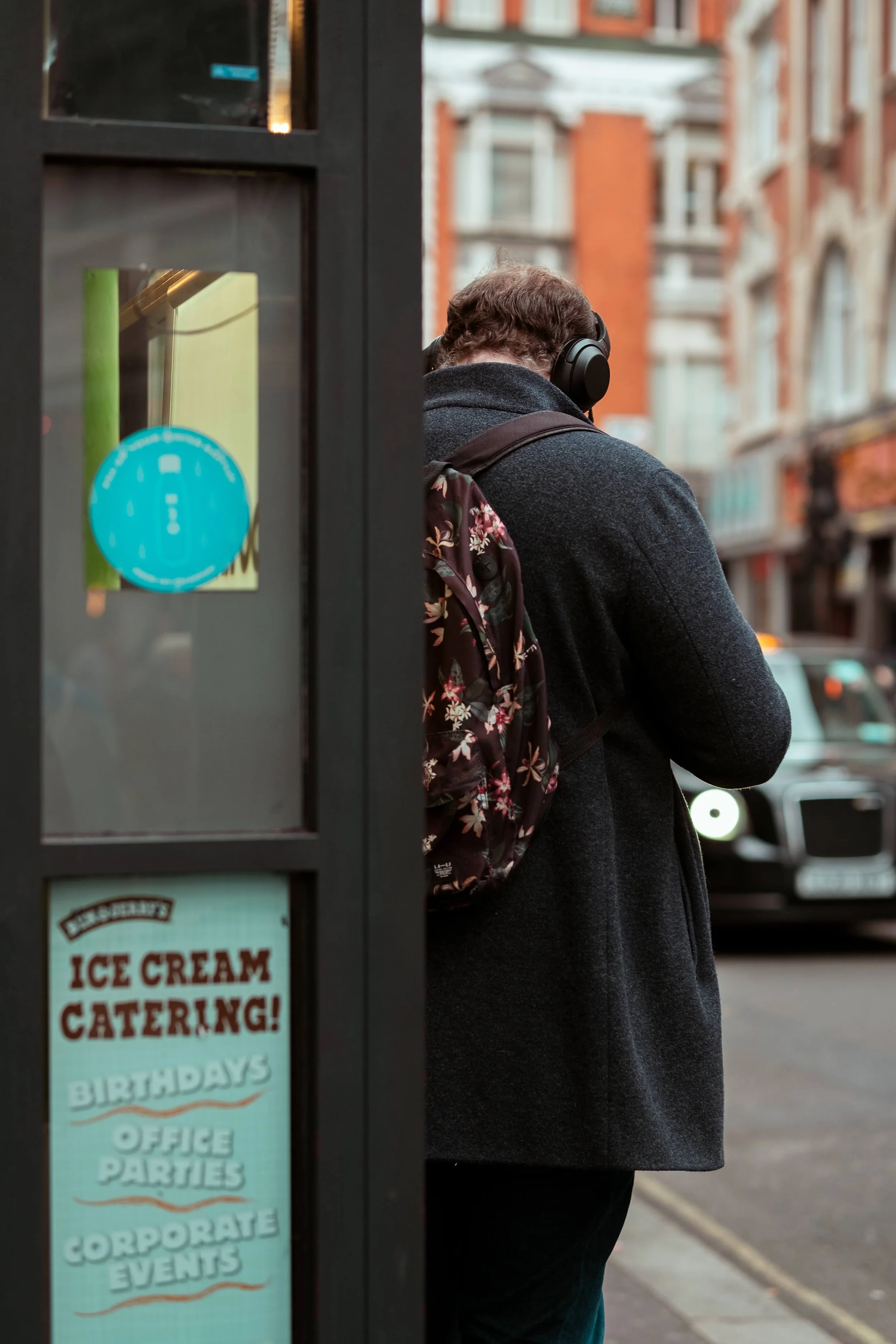 Person wearing headphones and a backpack standing outside a building.