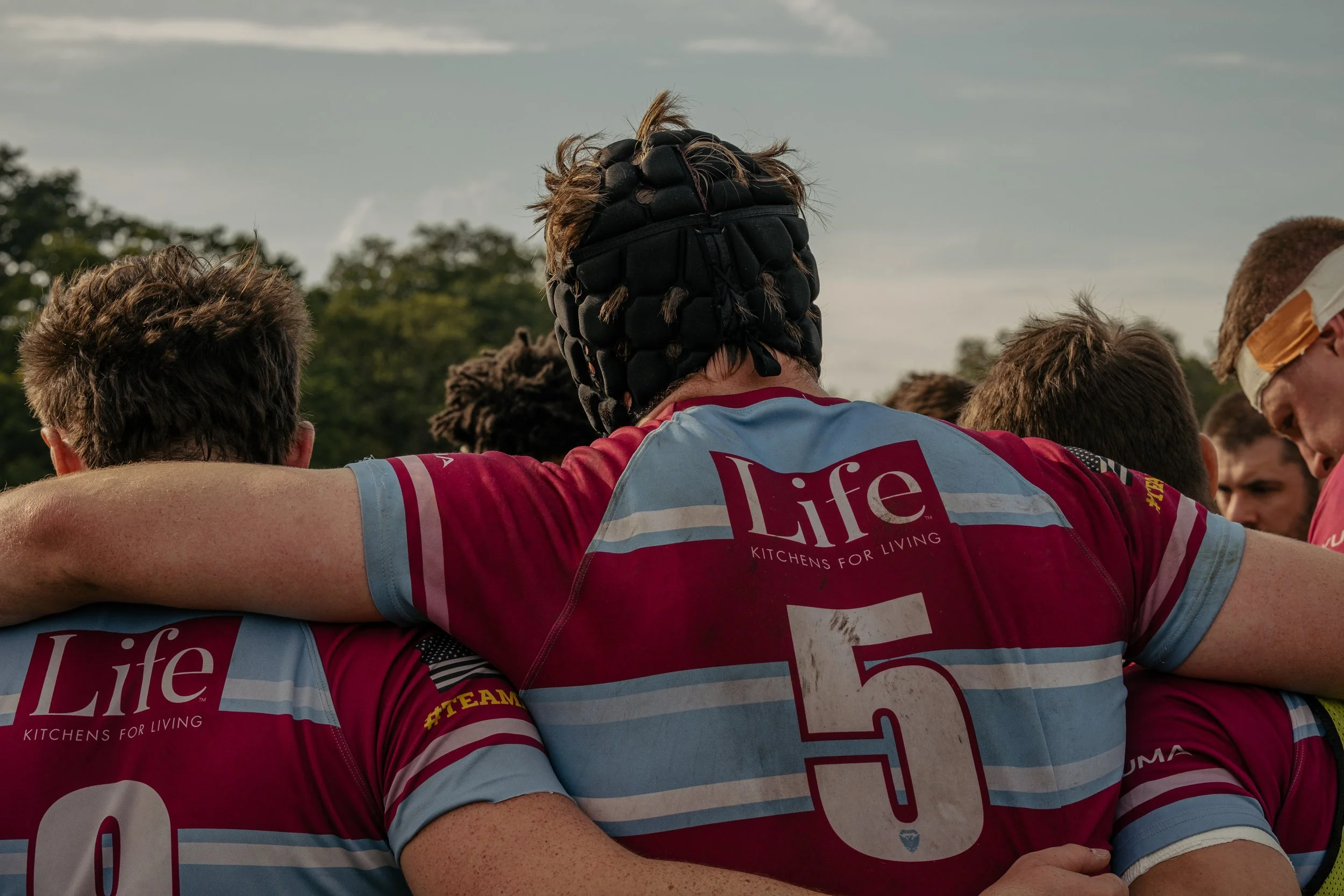Rugby players in a huddle, wearing red and blue jerseys with the word 'Life' and the number 5 on the back.