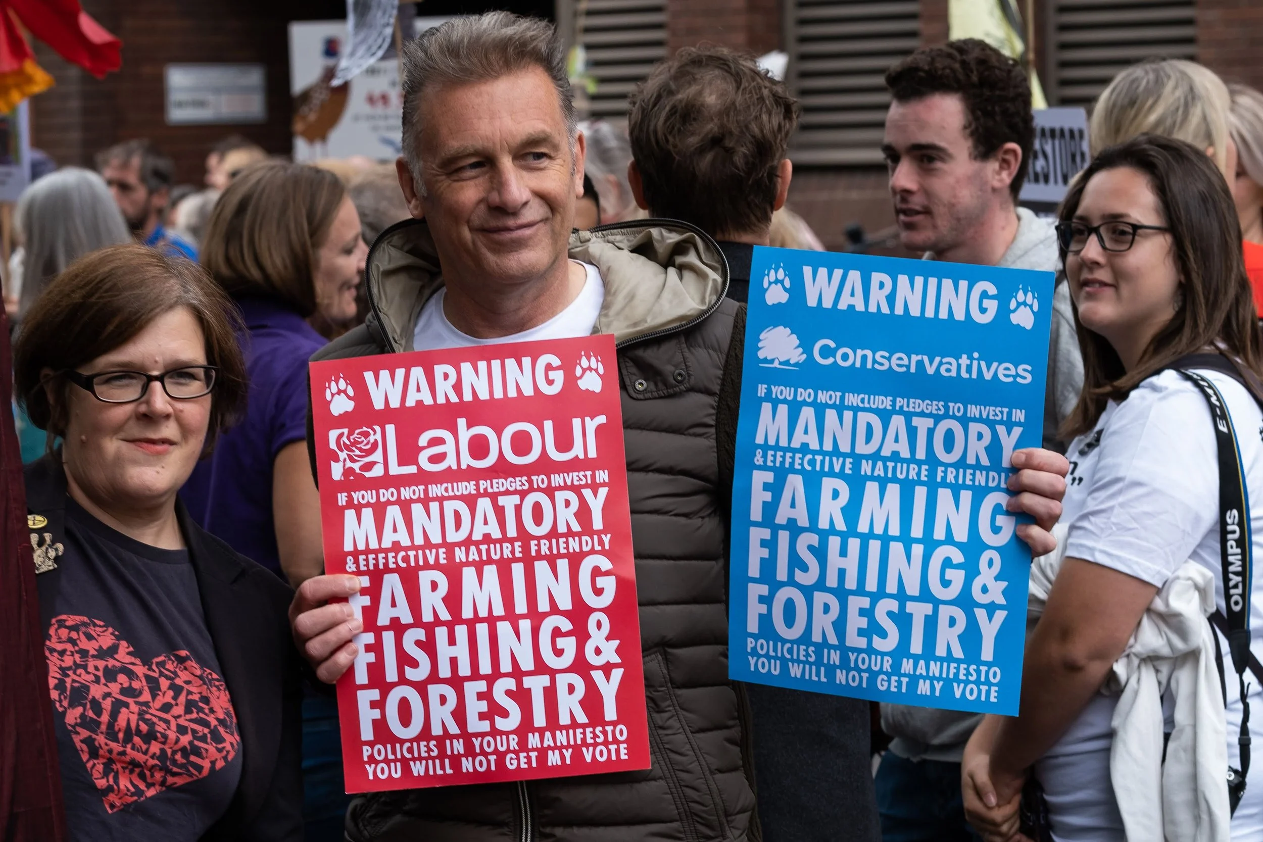 People at a protest holding signs that say warning about Labour and Conservatives, with messages about investment in farming, fishing, and forestry.