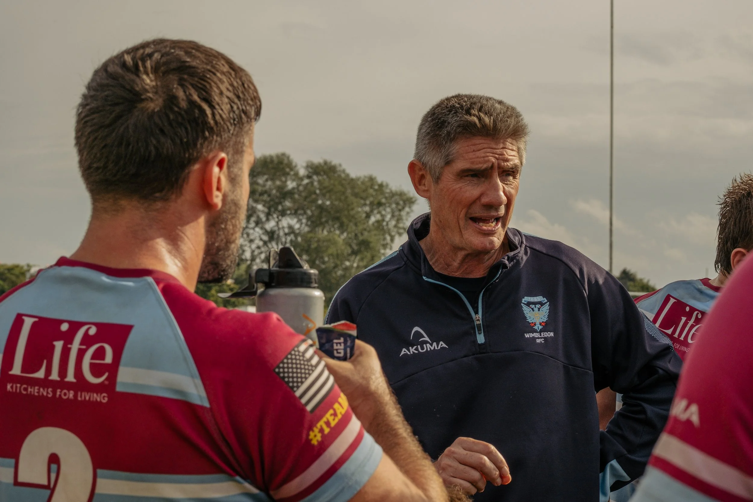 A man coaching rugby team during practice or game, speaking to players on the field.