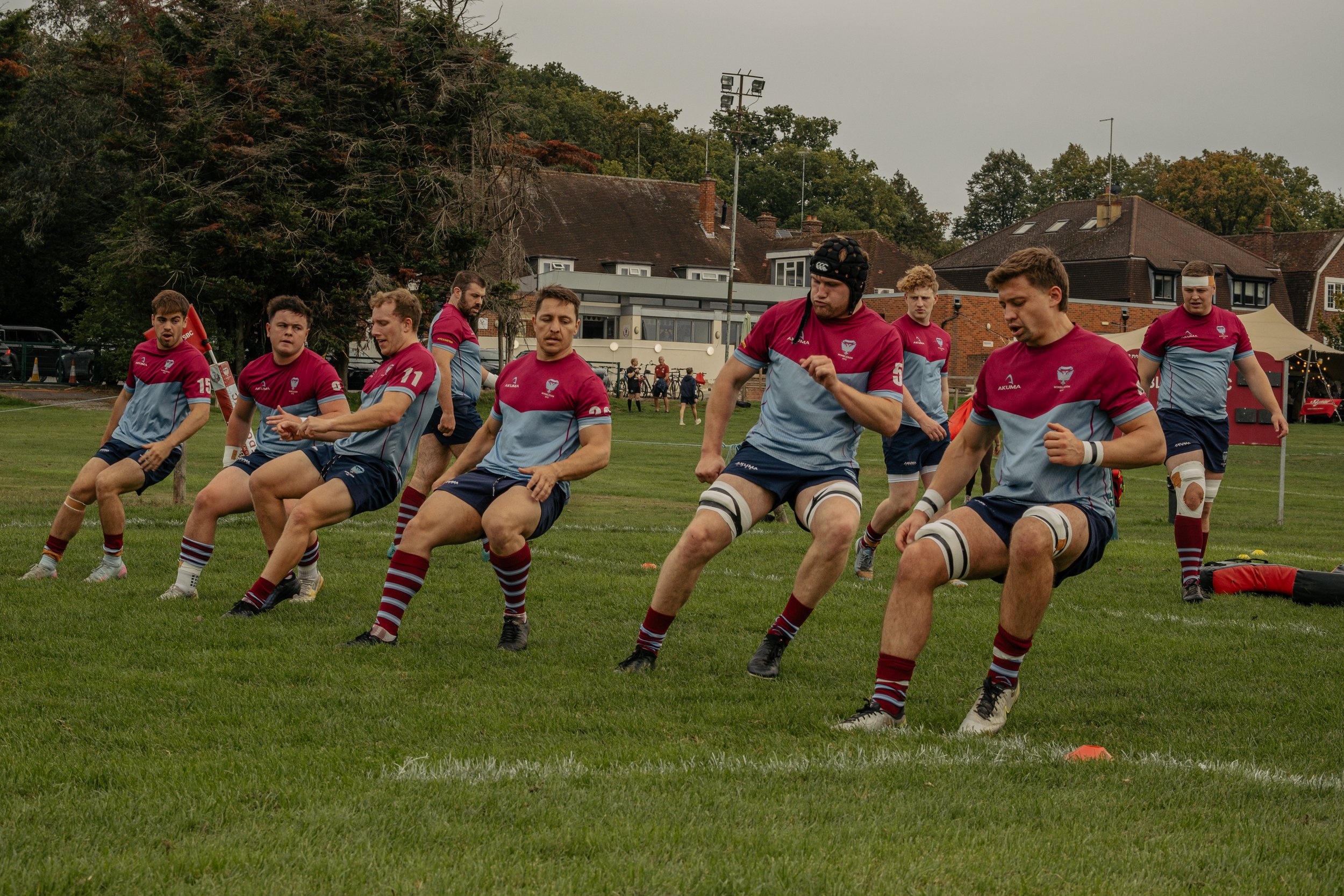 Rugby players practicing on a grassy field with houses and trees in the background