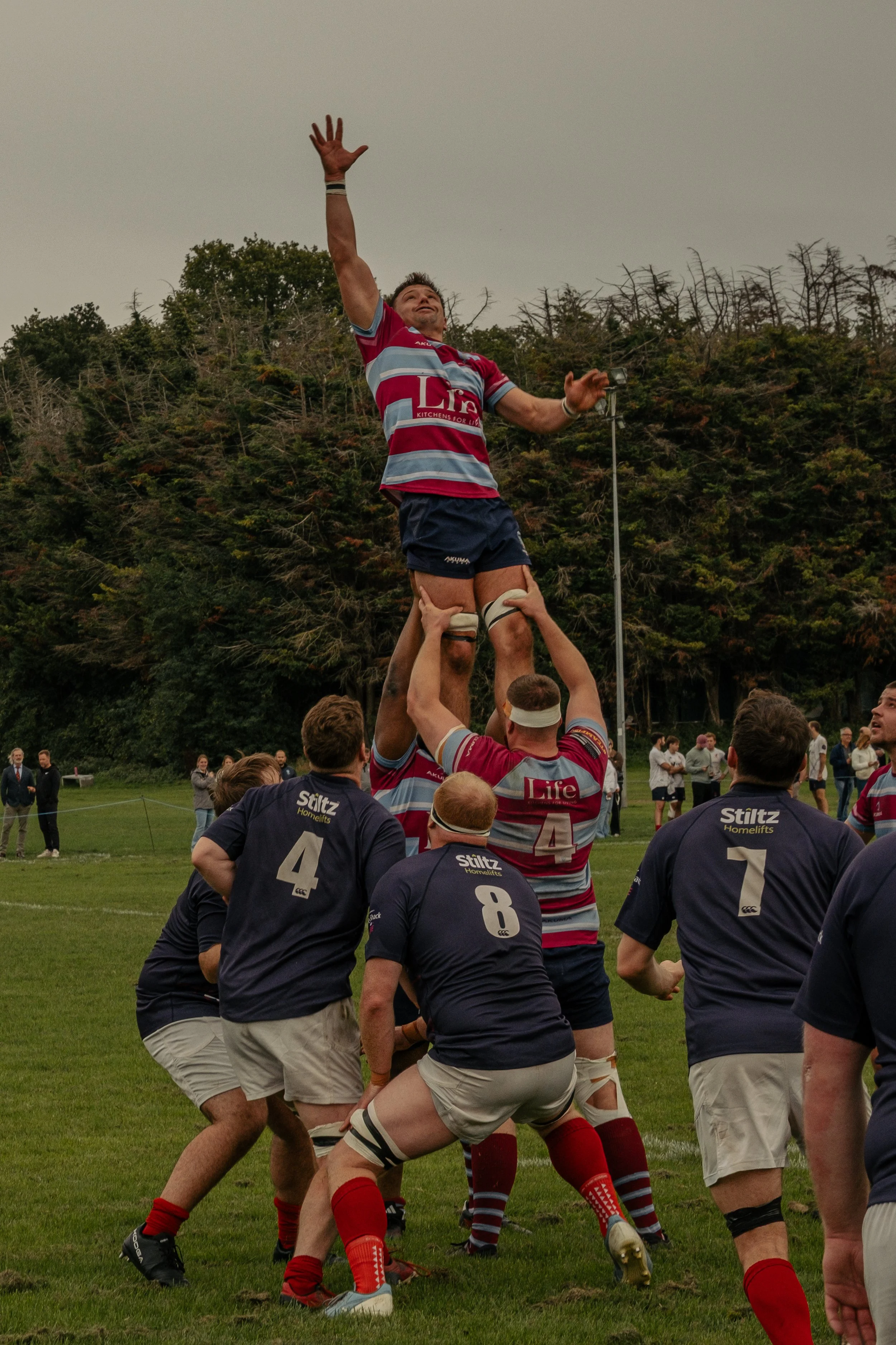 Rugby players performing a lineout during a match, with one player being lifted by teammates to catch the ball.