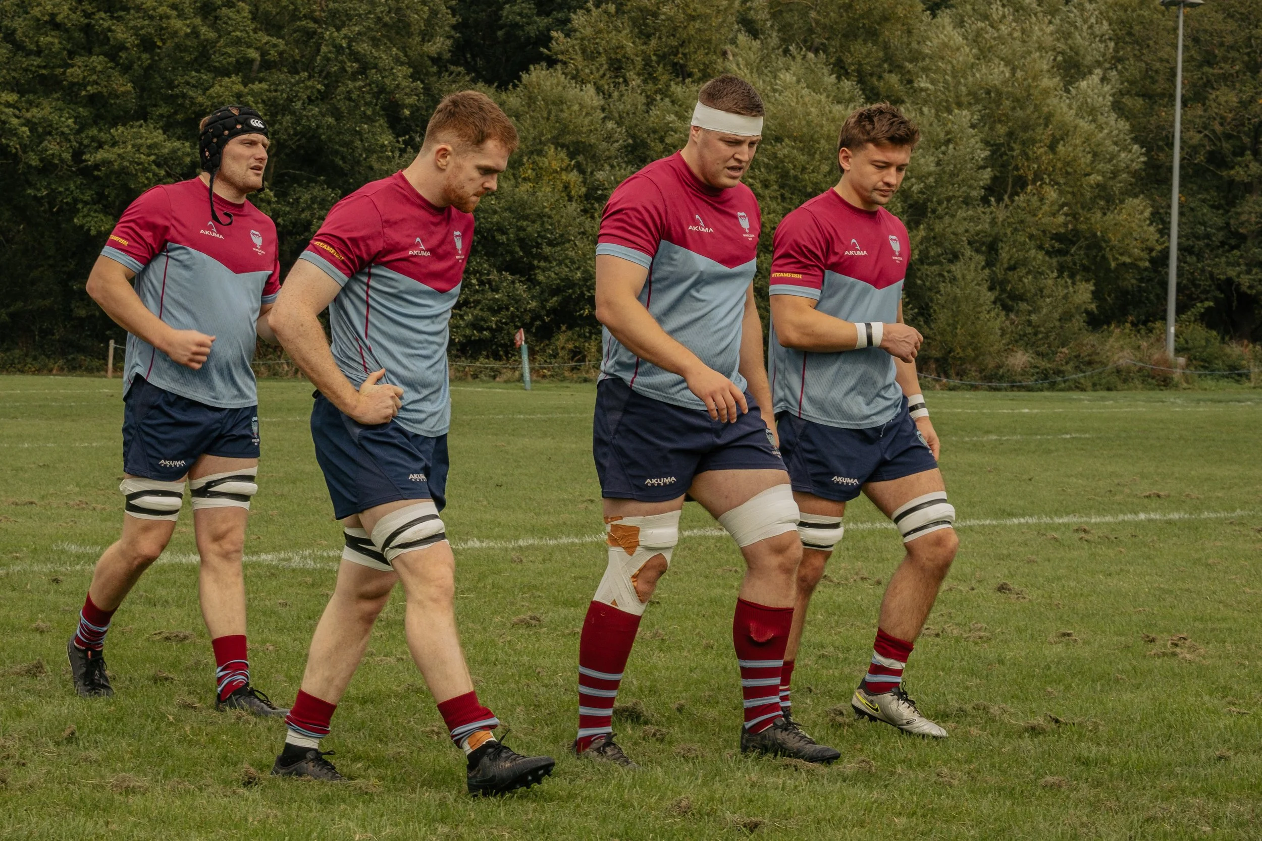 Rugby players walking on the field after injury, with one player having an ankle brace and tape.