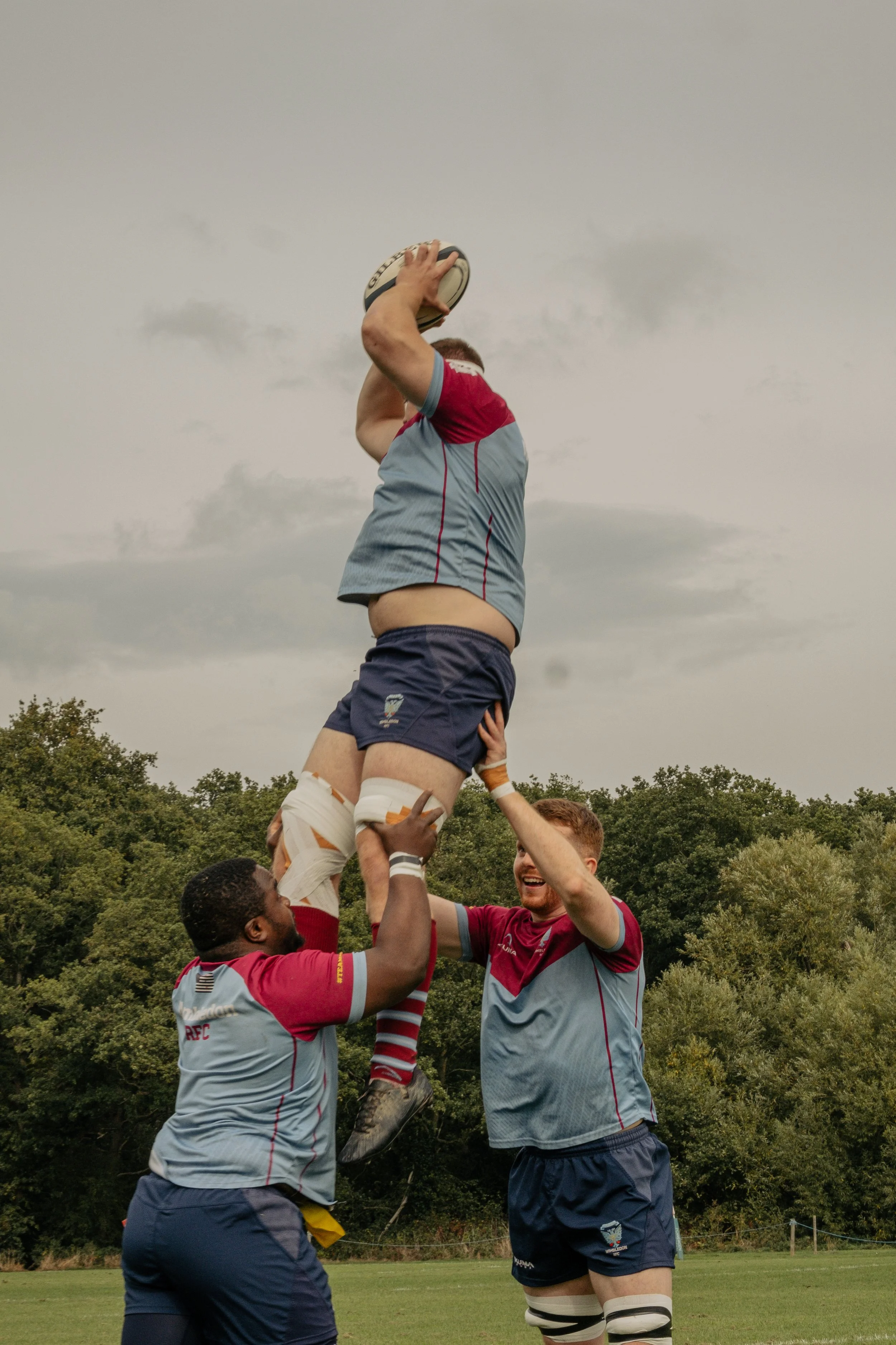 Rugby players performing a line-out lift during a game, with one player reaching to catch the ball.