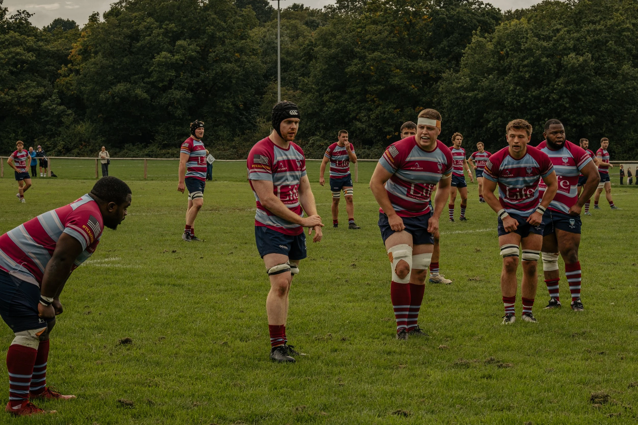 Rugby players in maroon and blue striped uniforms on a grassy field during a match.