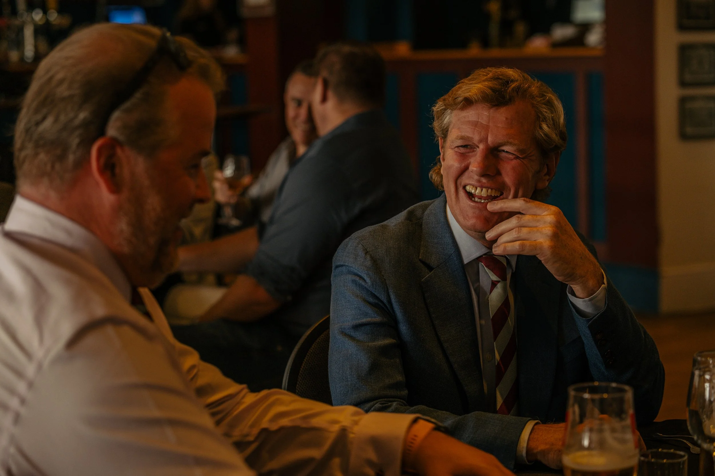 People sitting and chatting at a bar or restaurant, smiling and laughing, socializing in a cozy, dimly lit setting.