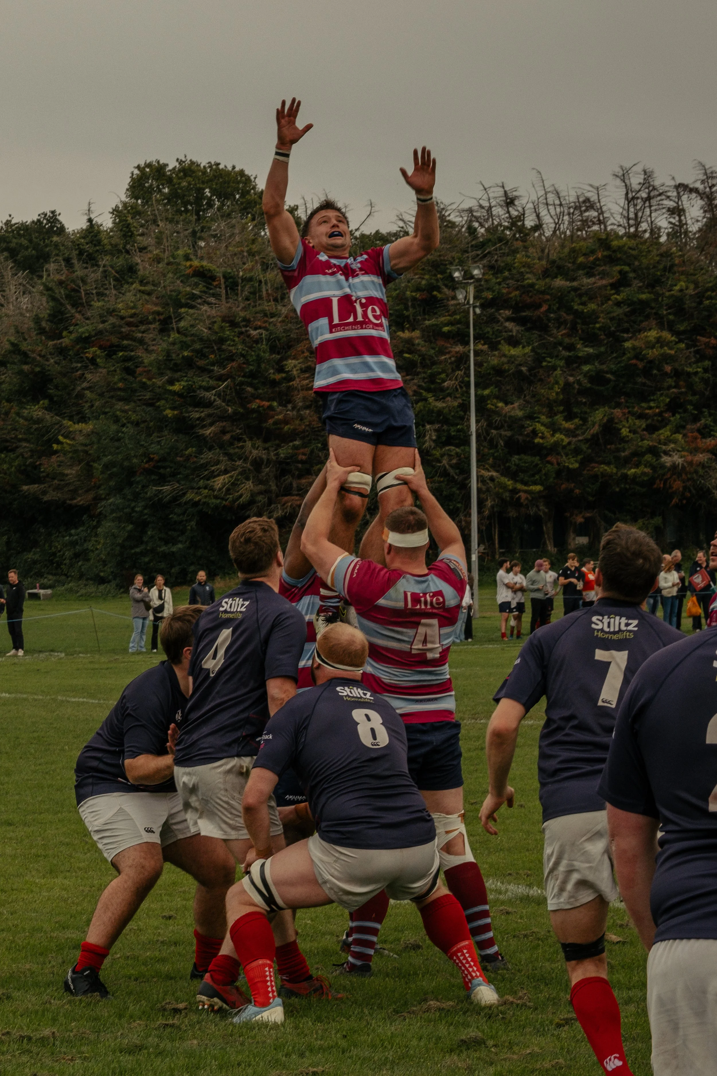 Rugby players performing a line-out formation during a match, with one player being lifted by his teammates to catch the ball.