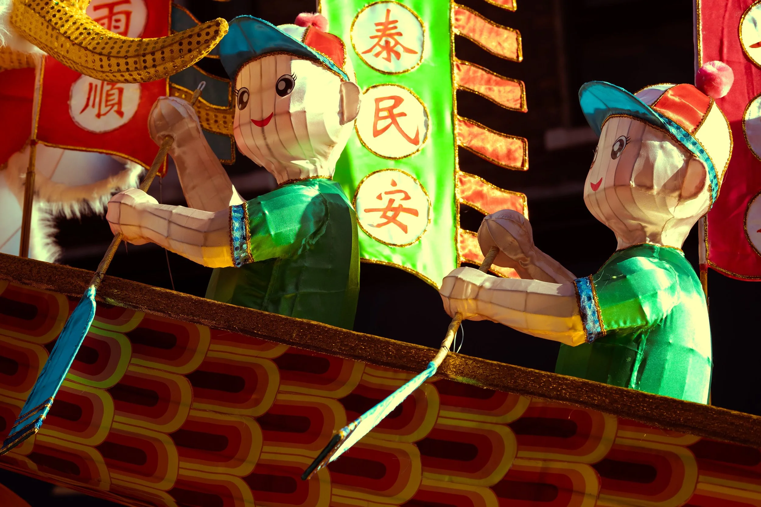Colorful lanterns with two smiling child figures dressed in green, holding sticks, part of a festive display at night.