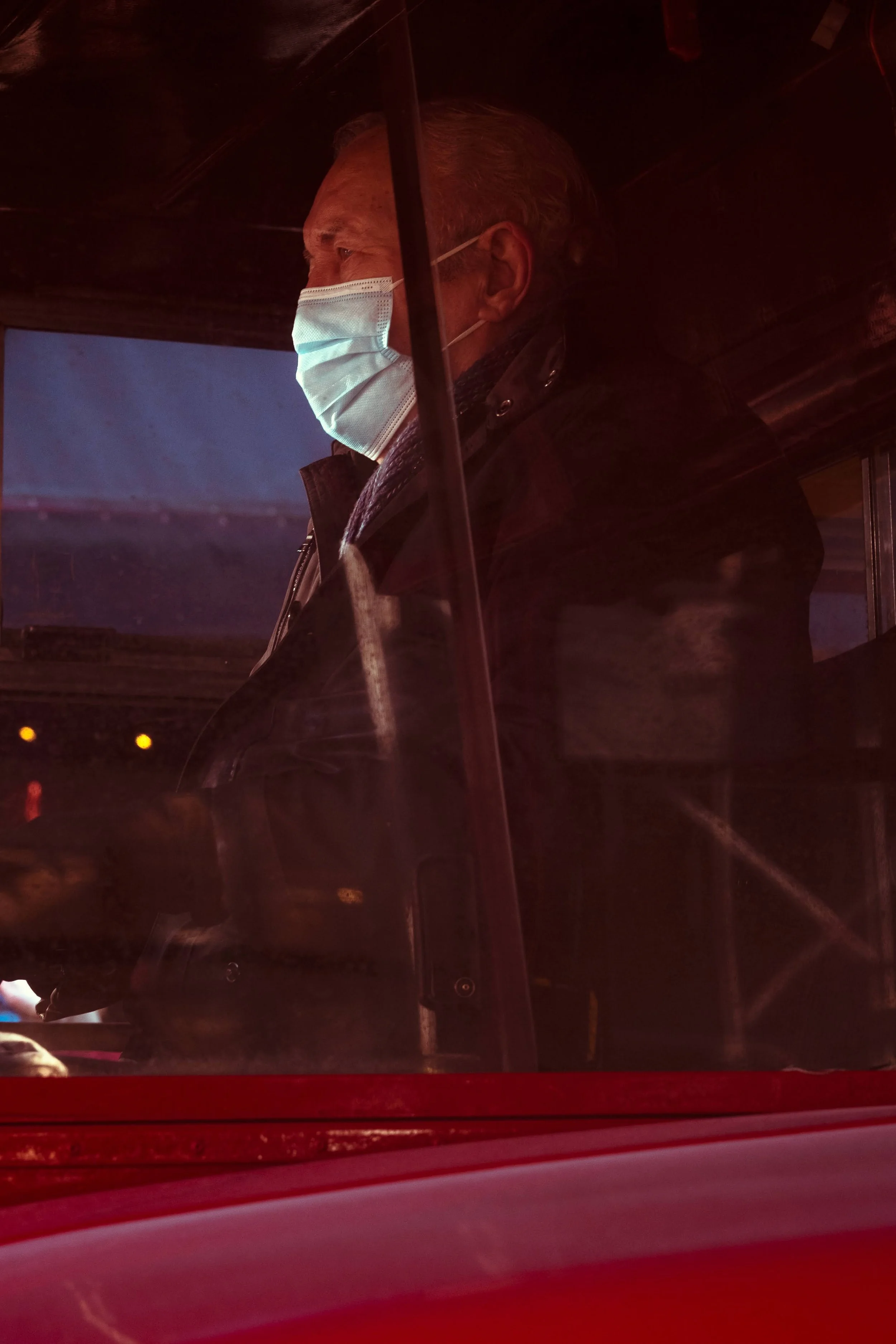 Side view of a man wearing a mask, standing inside a vehicle, illuminated by red and blue lighting.