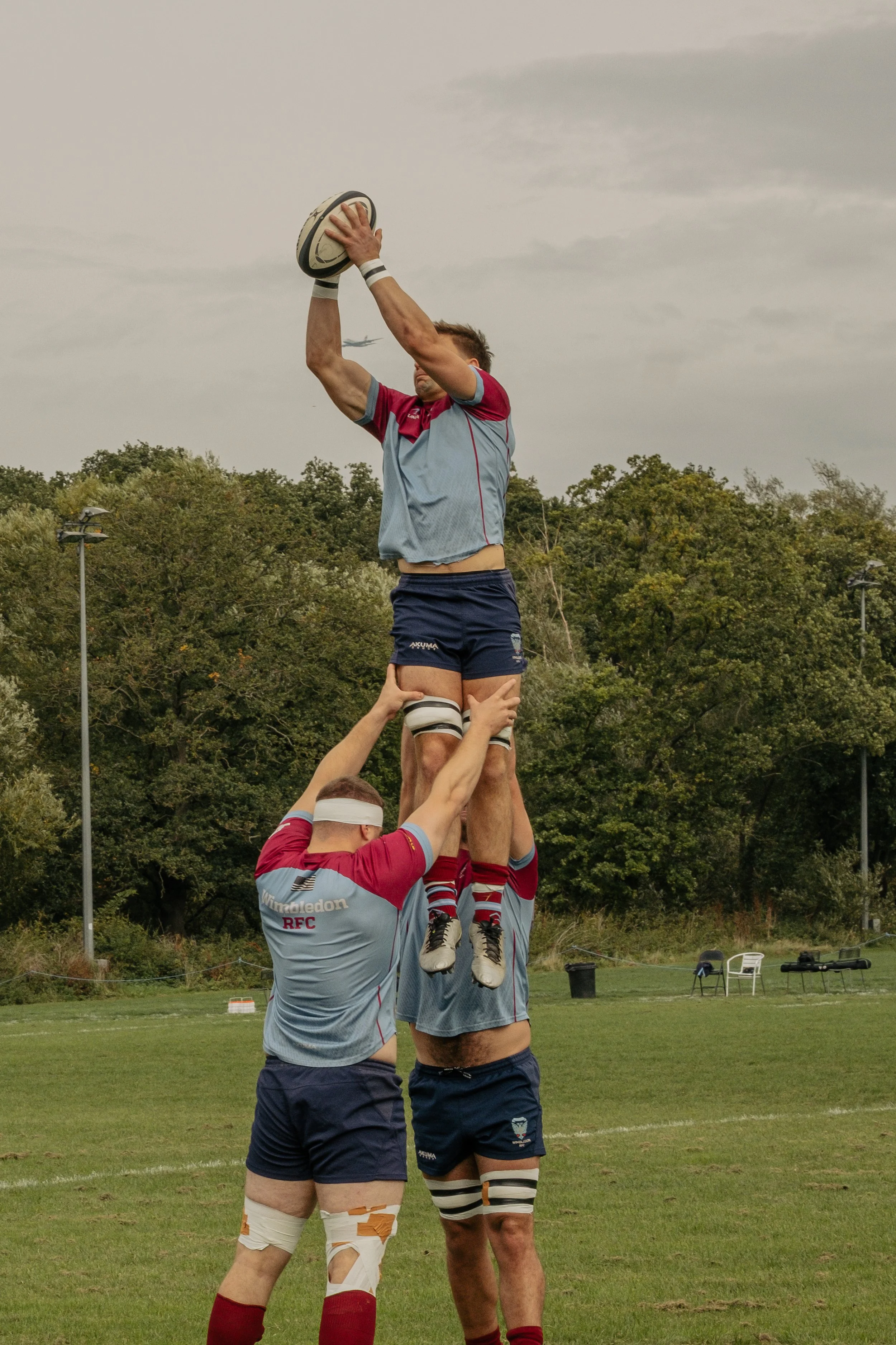 A group of rugby players forming a human pyramid on a grassy field, with one player at the top holding a rugby ball above their head.