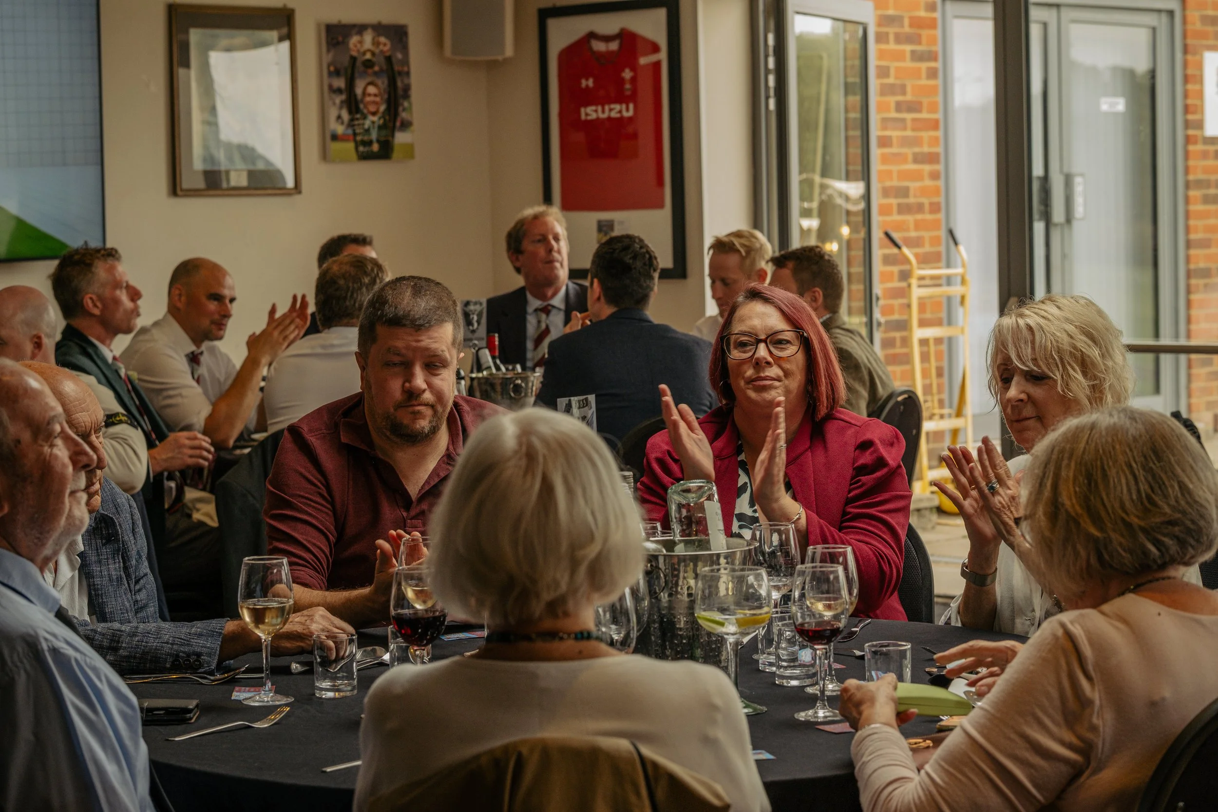 A group of people seated around a dining table, clapping and engaging in a social event or celebration at a restaurant or banquet hall.