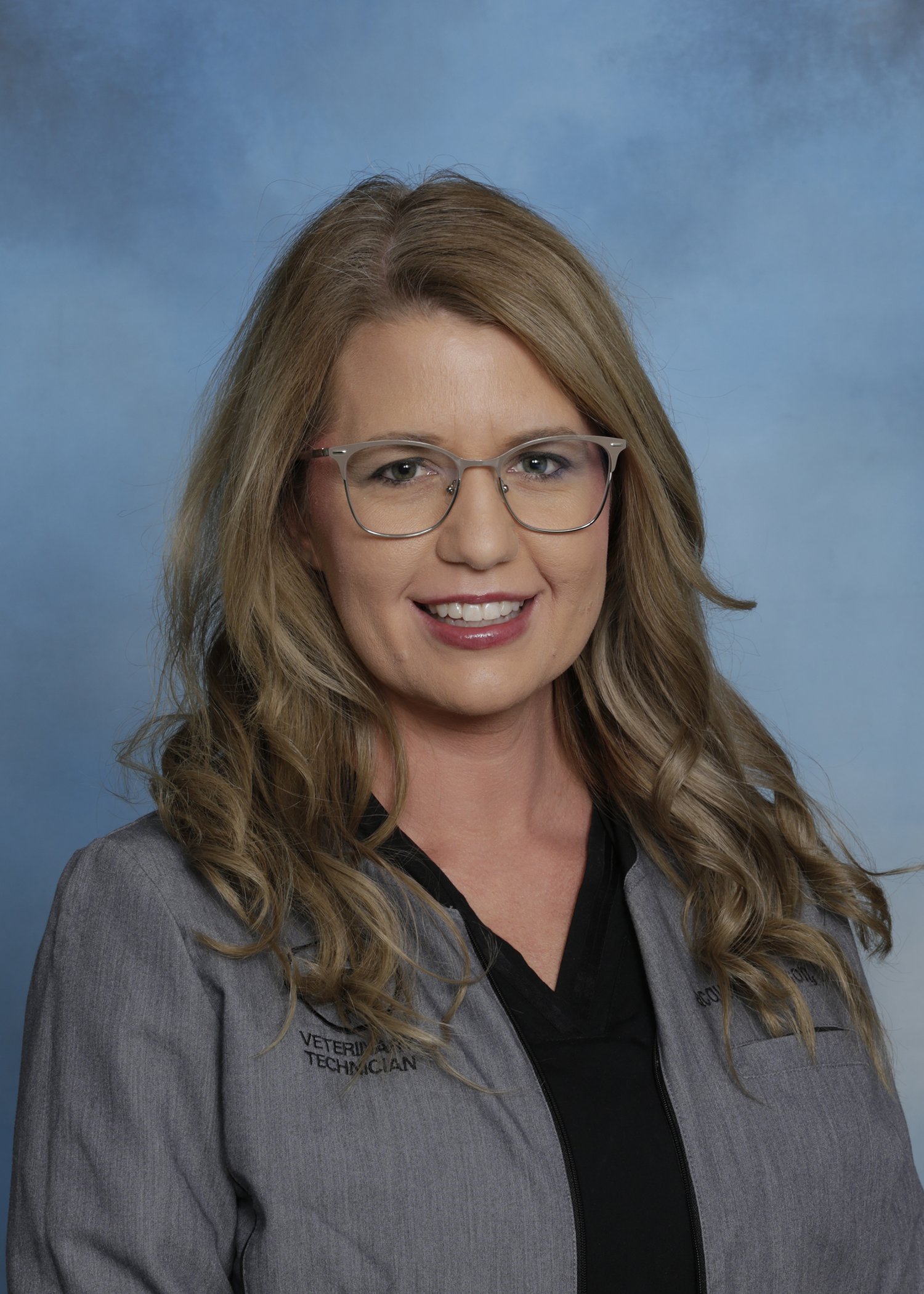 Middle-aged man with glasses wearing blue medical scrubs standing against a light-colored wall.