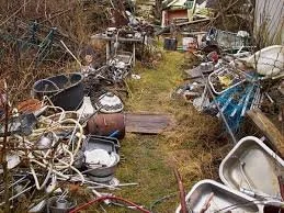 A cluttered yard with numerous old, discarded bicycles, wheels, and miscellaneous metal and plastic items scattered around.