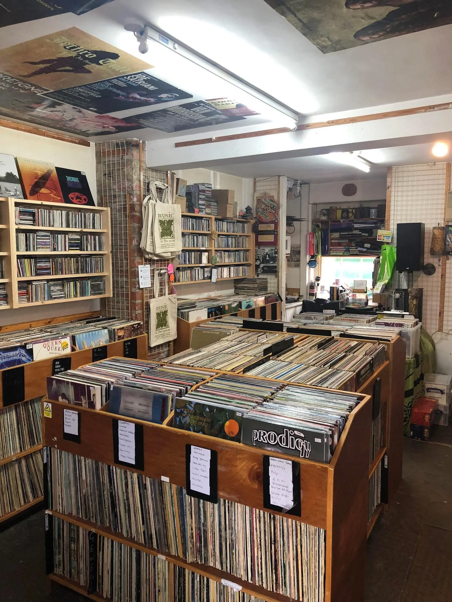 Interior of Music in the Green's Bakewell shop with wooden browser boxes filled with vinyl records. There are CDs on the racks and gig posters on the ceiling - the interior has a traditional record shop feel.