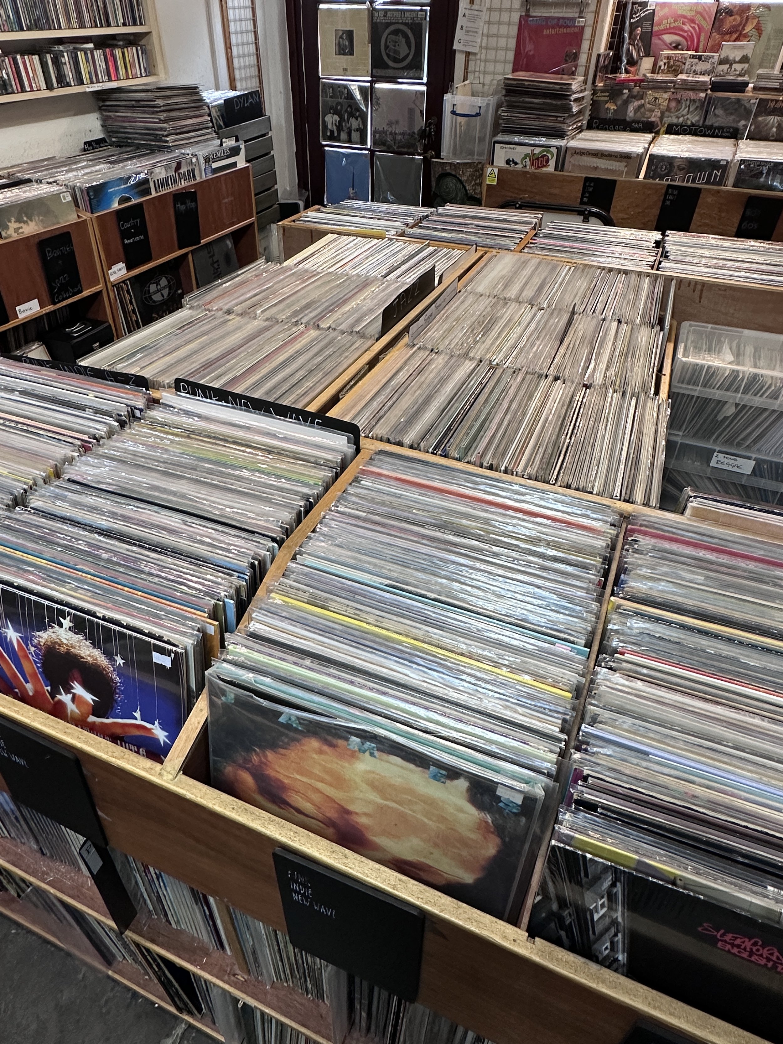 Interior of Music in the Green's Bakewell shop, with a display of stacked vinyl records. There are CDs on the racks and gig posters on the ceiling - the interior has a traditional record shop feel.