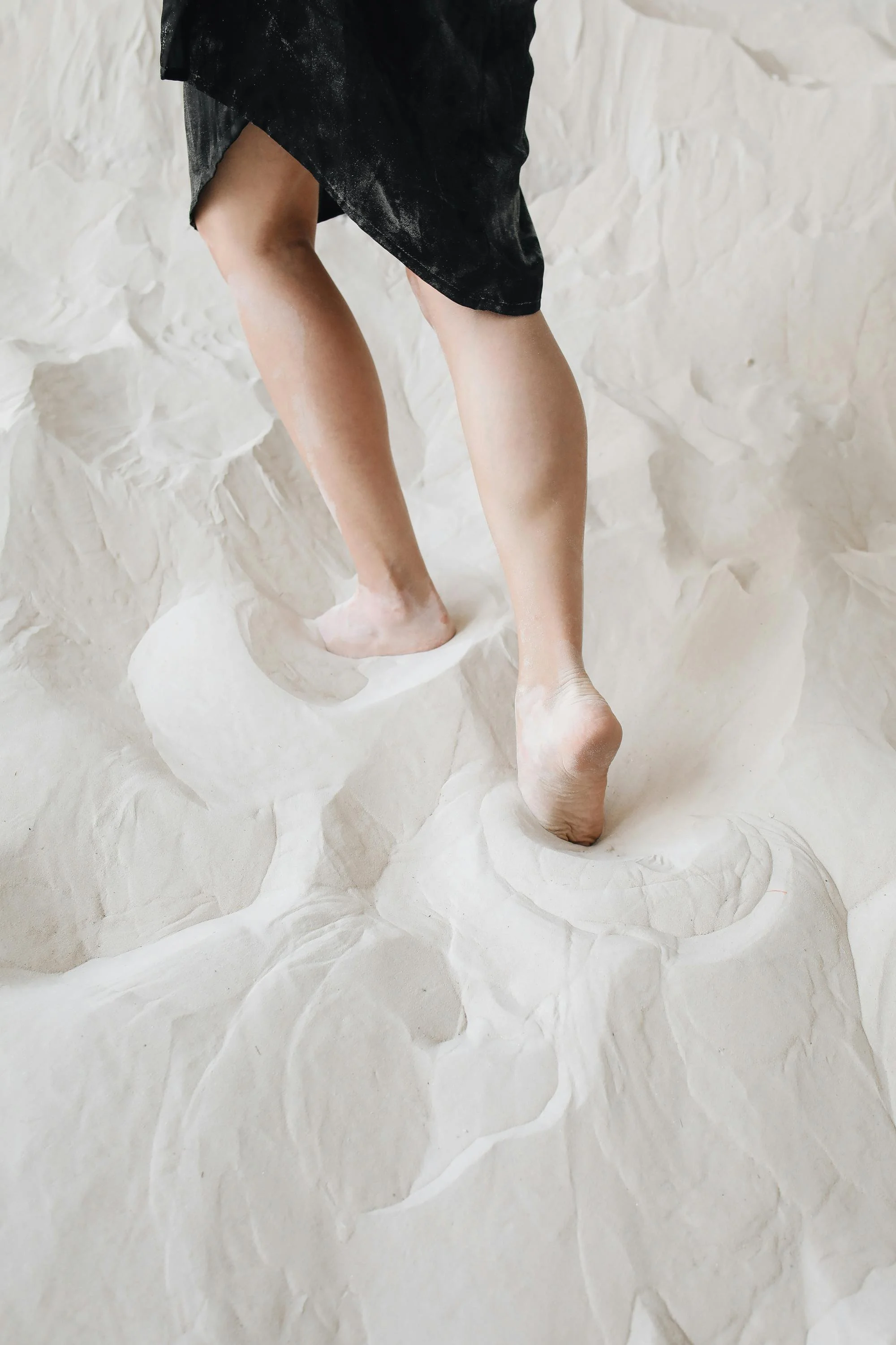 Person walking barefoot on a textured white surface, wearing a black garment.
