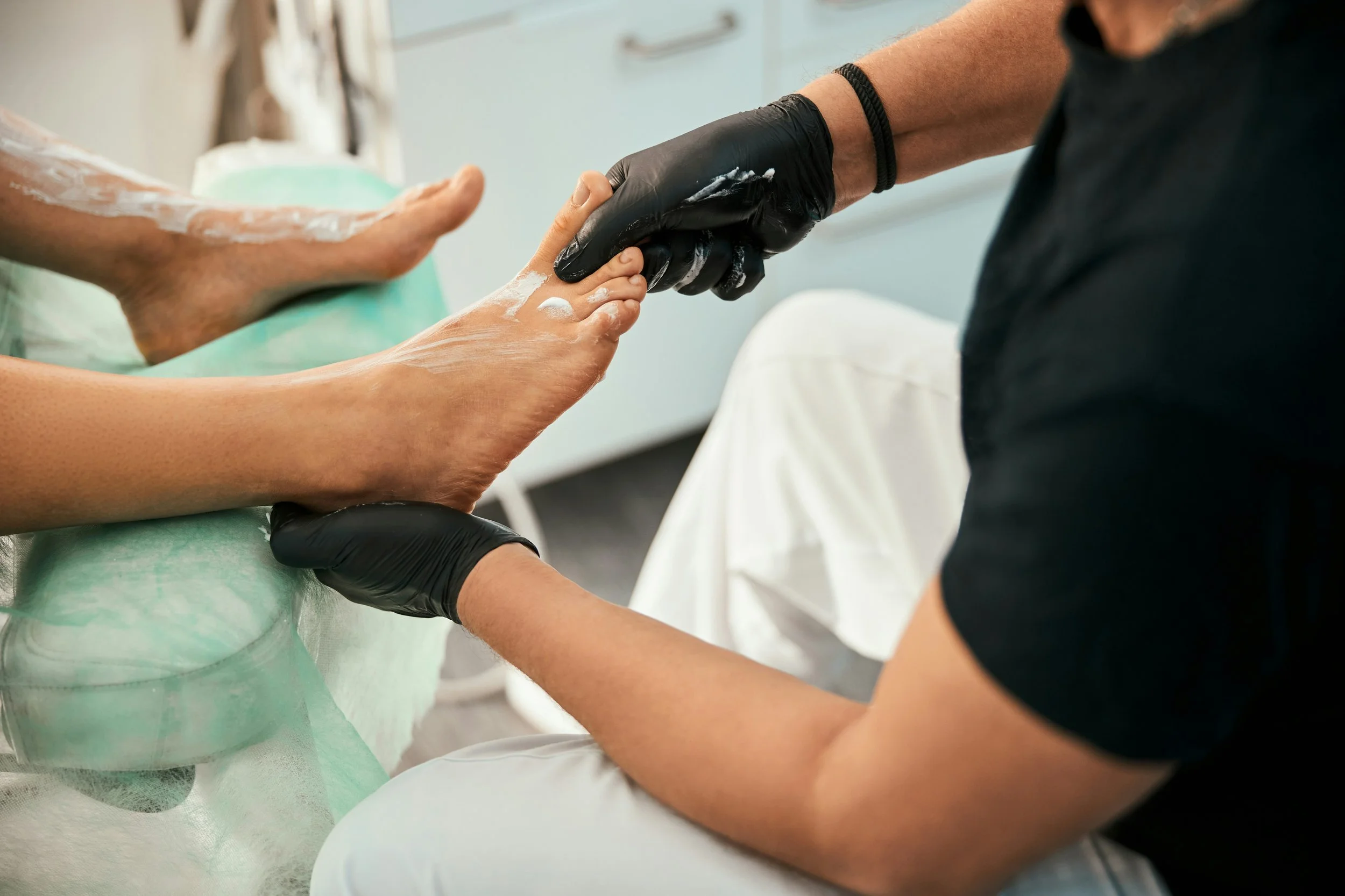 A person wearing black gloves holding a patient's feet during a medical or spa treatment.