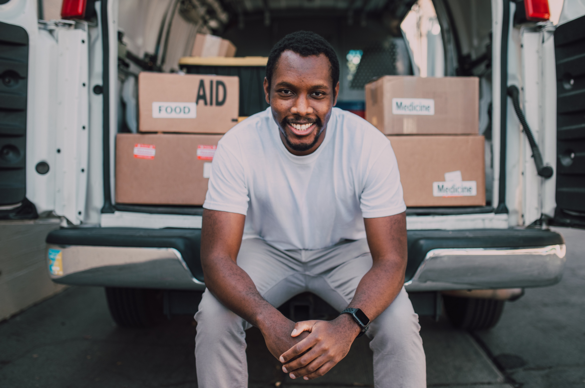 A man sits on the rear of a truck which is providing cardboard boxes of Aid relief.