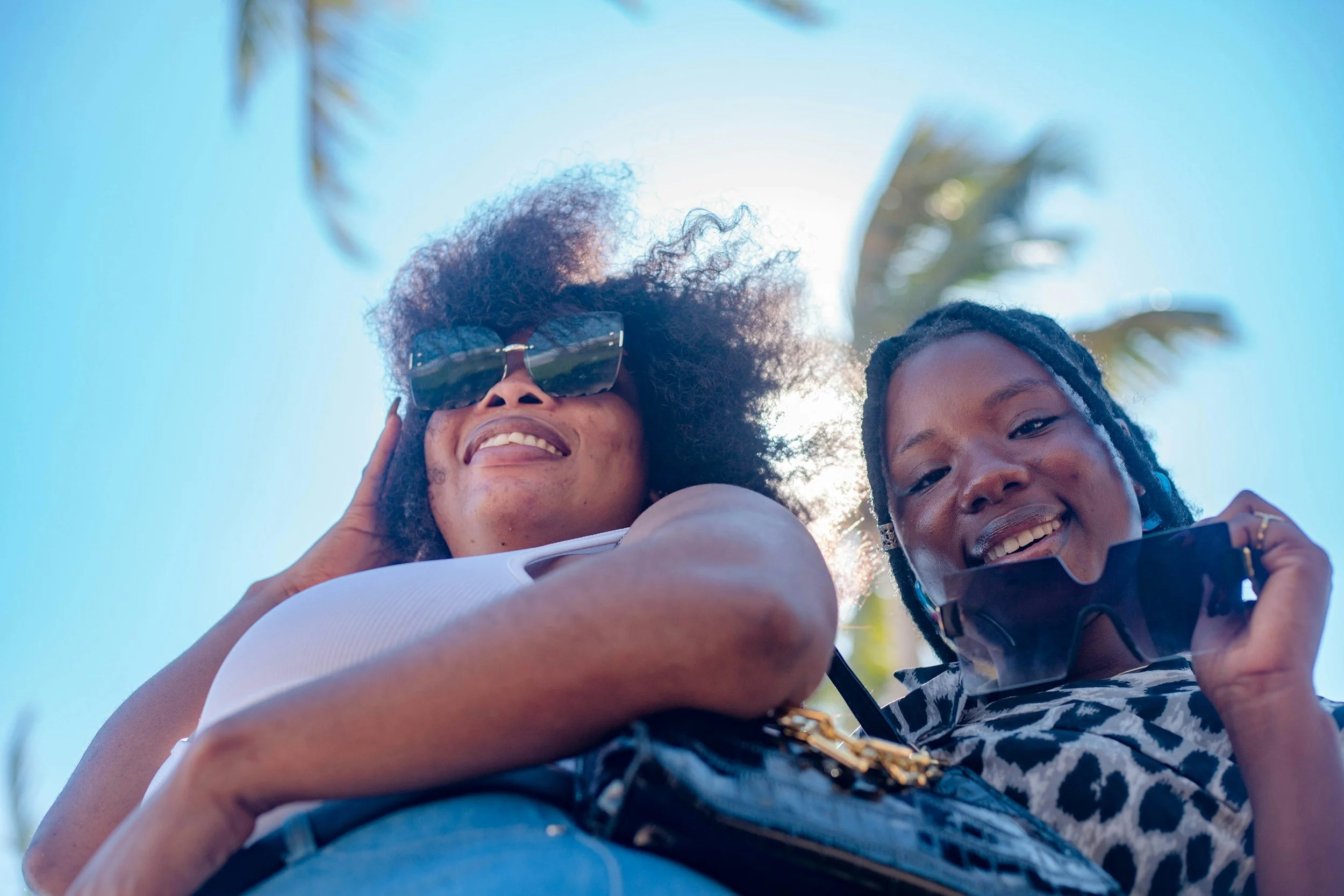 An older woman and teenage girl stand in front of a palm tree, smiling.
