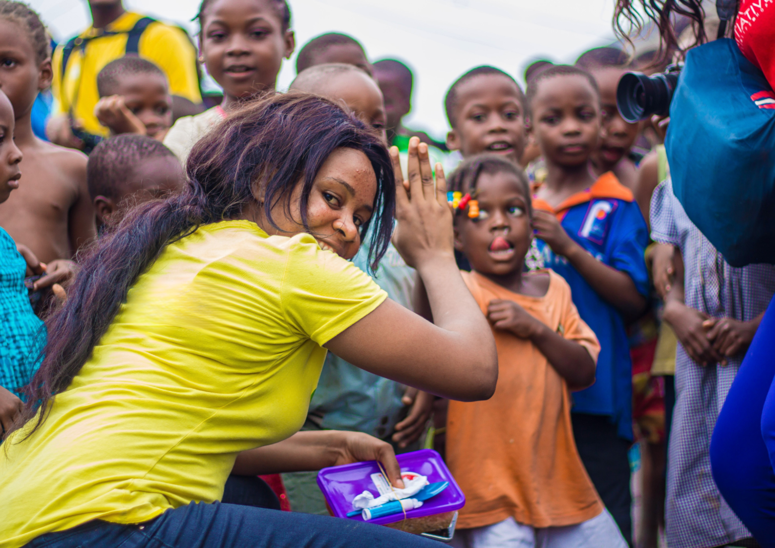 A woman in a lime green t-shirt gives a high five to a young African boy who stands among a whole group of kids in front of the woman, who is most likely a volunteer. working with the kids
