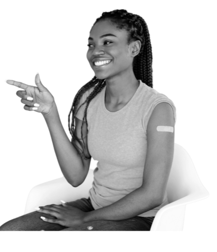 A young woman with braids has a band-aid on her right shoulder, smiles and points.