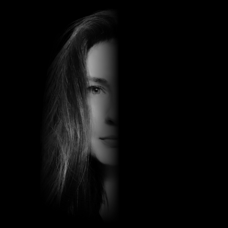 Half of a woman's face with long hair visible, black and white photo with dark background.