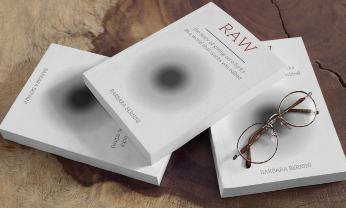 Three books with blurred black circles on the covers and a pair of round eyeglasses resting on one of the books, all on a wooden surface.