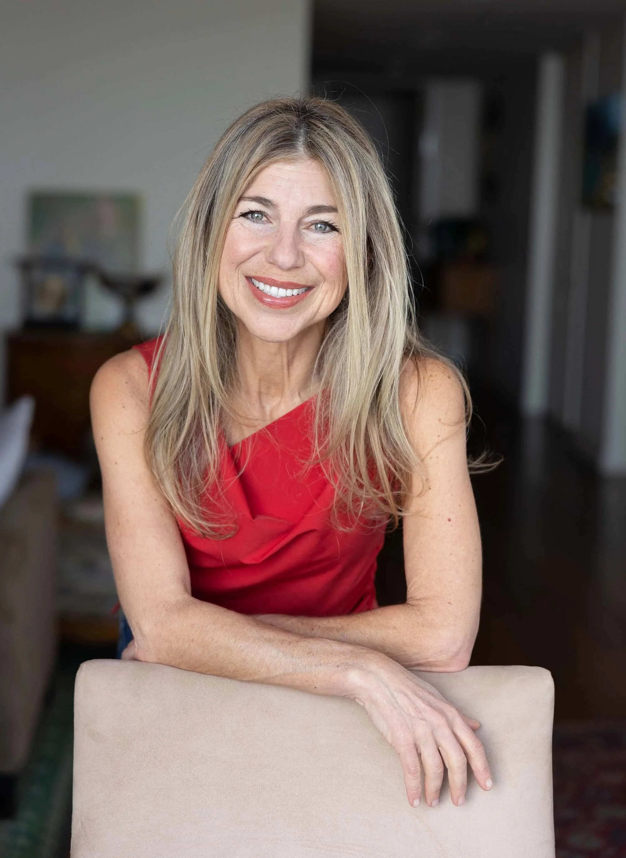 Woman in red sleeveless dress smiling warmly at the camera in an indoor setting