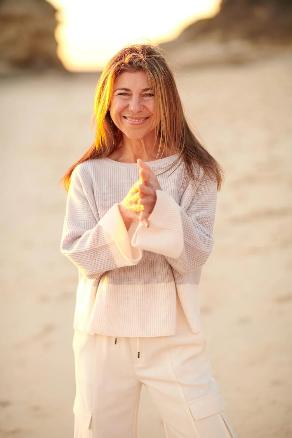 Woman in white ribbed sweater smiling warmly outdoors in golden hour sunlight