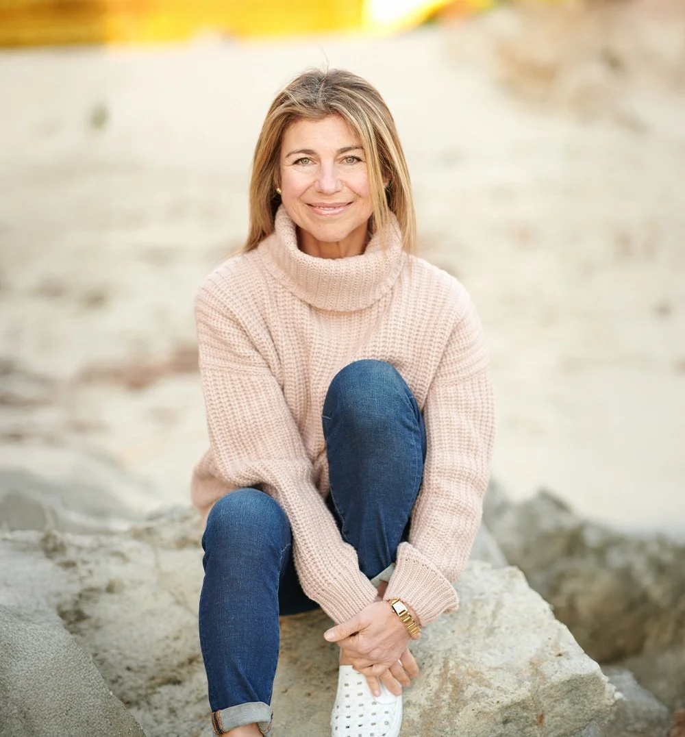 Woman in beige turtleneck sweater smiling warmly outdoors