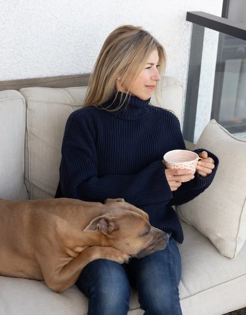 Woman relaxing on a couch with her dog, holding a cup of tea.