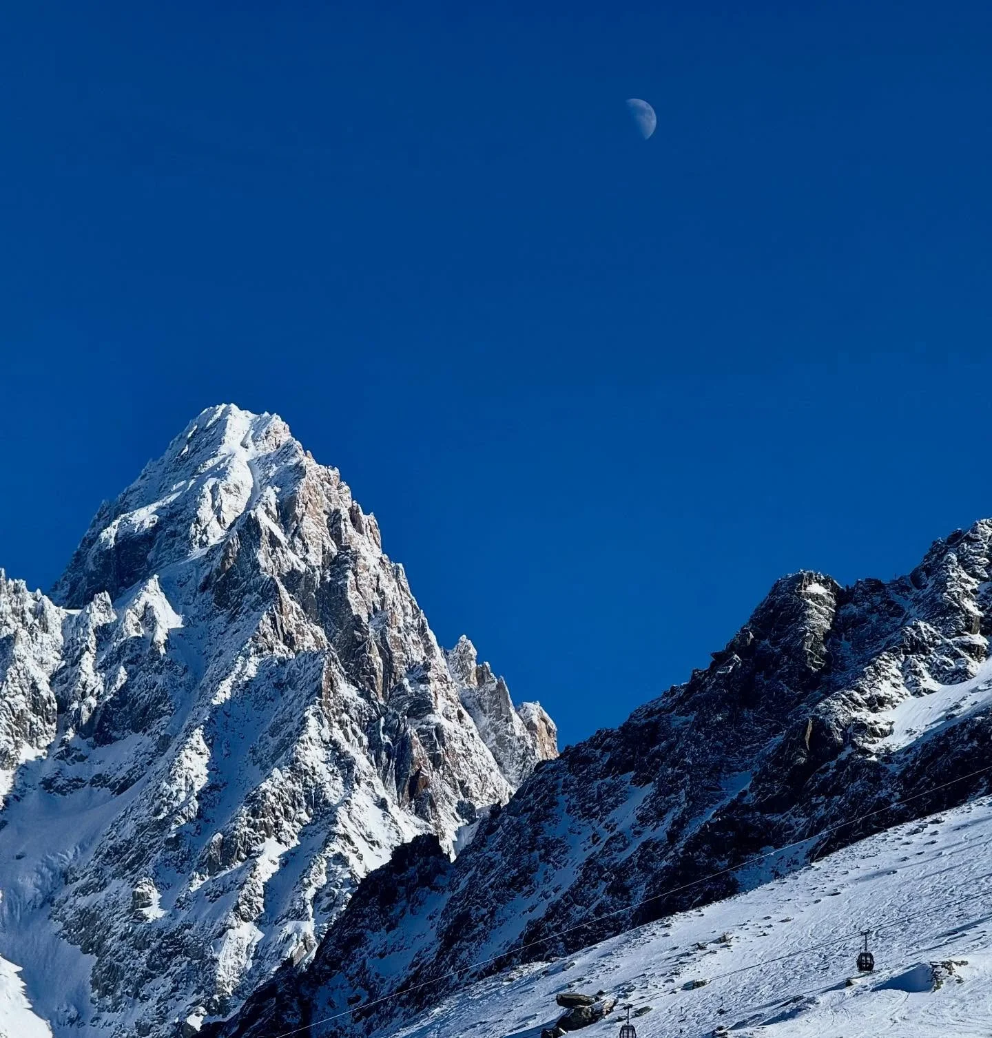 Half moon drifting over the mountains at midday.