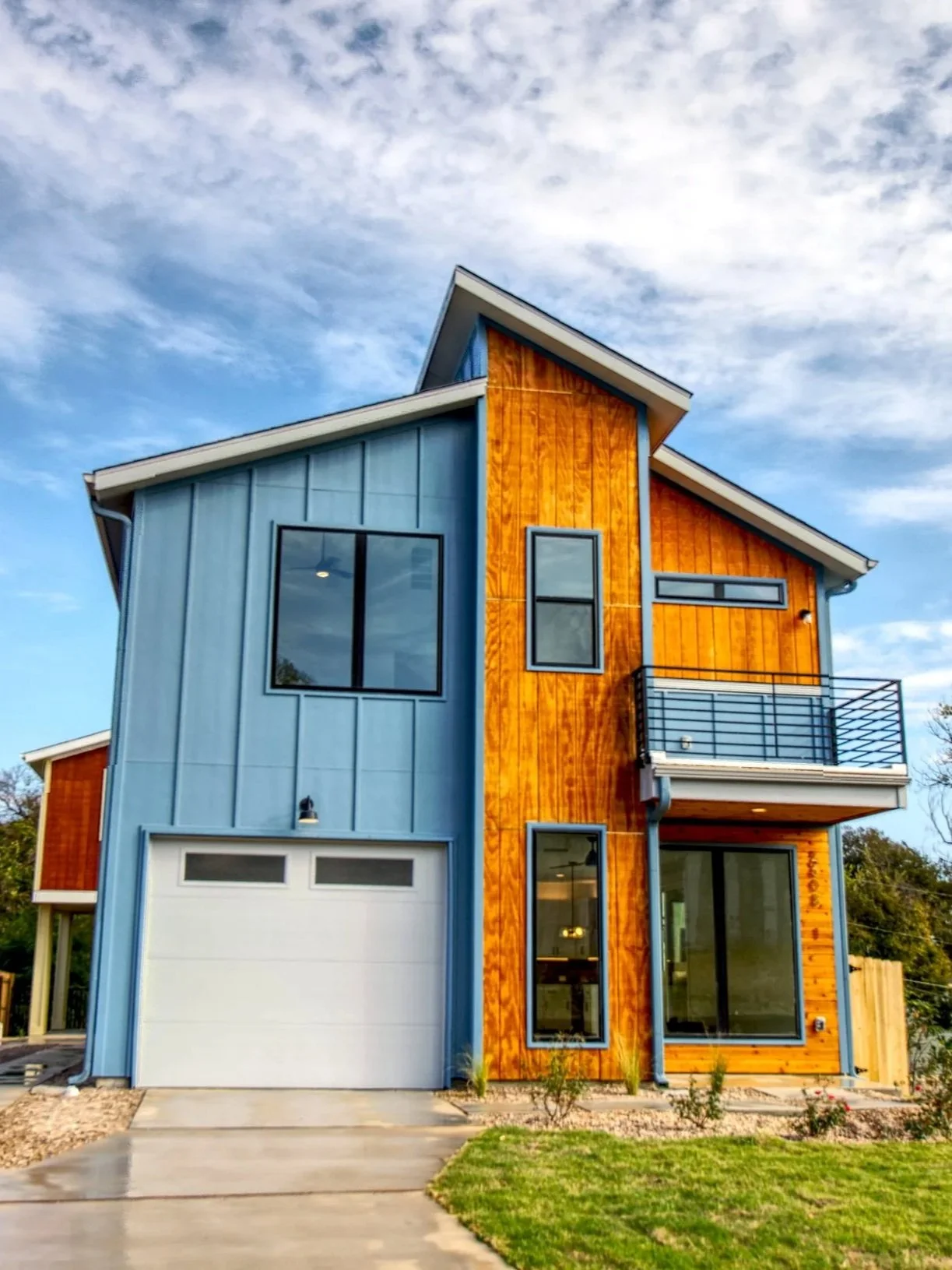 Modern two-story house with a blue and wood exterior, large windows, and a small front yard.