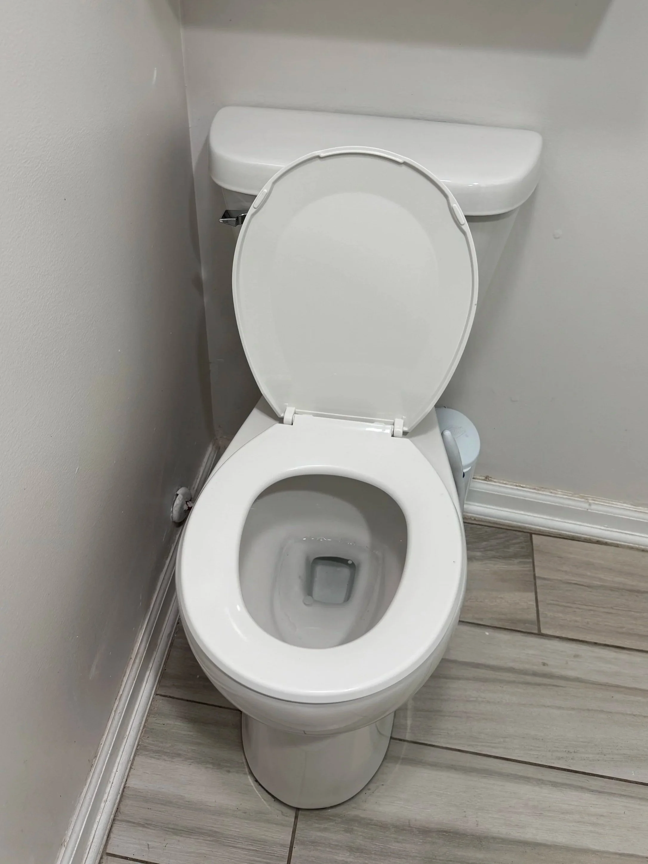 White toilet with open lid in a bathroom with beige tile floor and white walls.