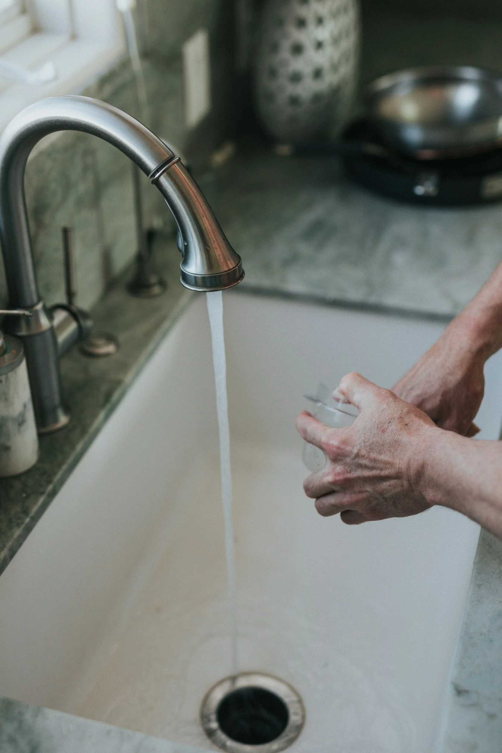 Person washing a glass in a kitchen sink with running water.