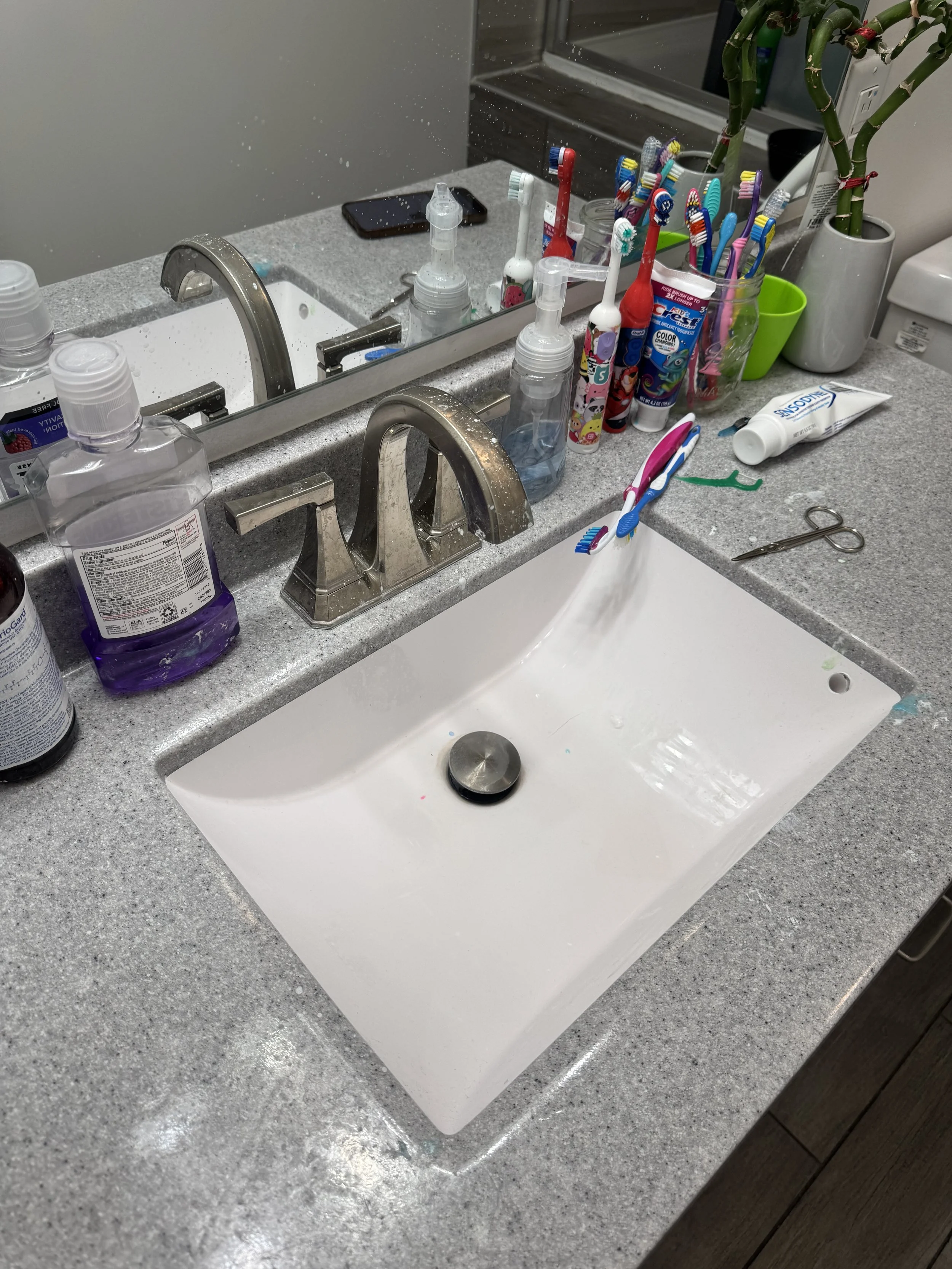 Bathroom sink with various toothbrushes, toothpaste, soap, and toiletries on the countertop.
