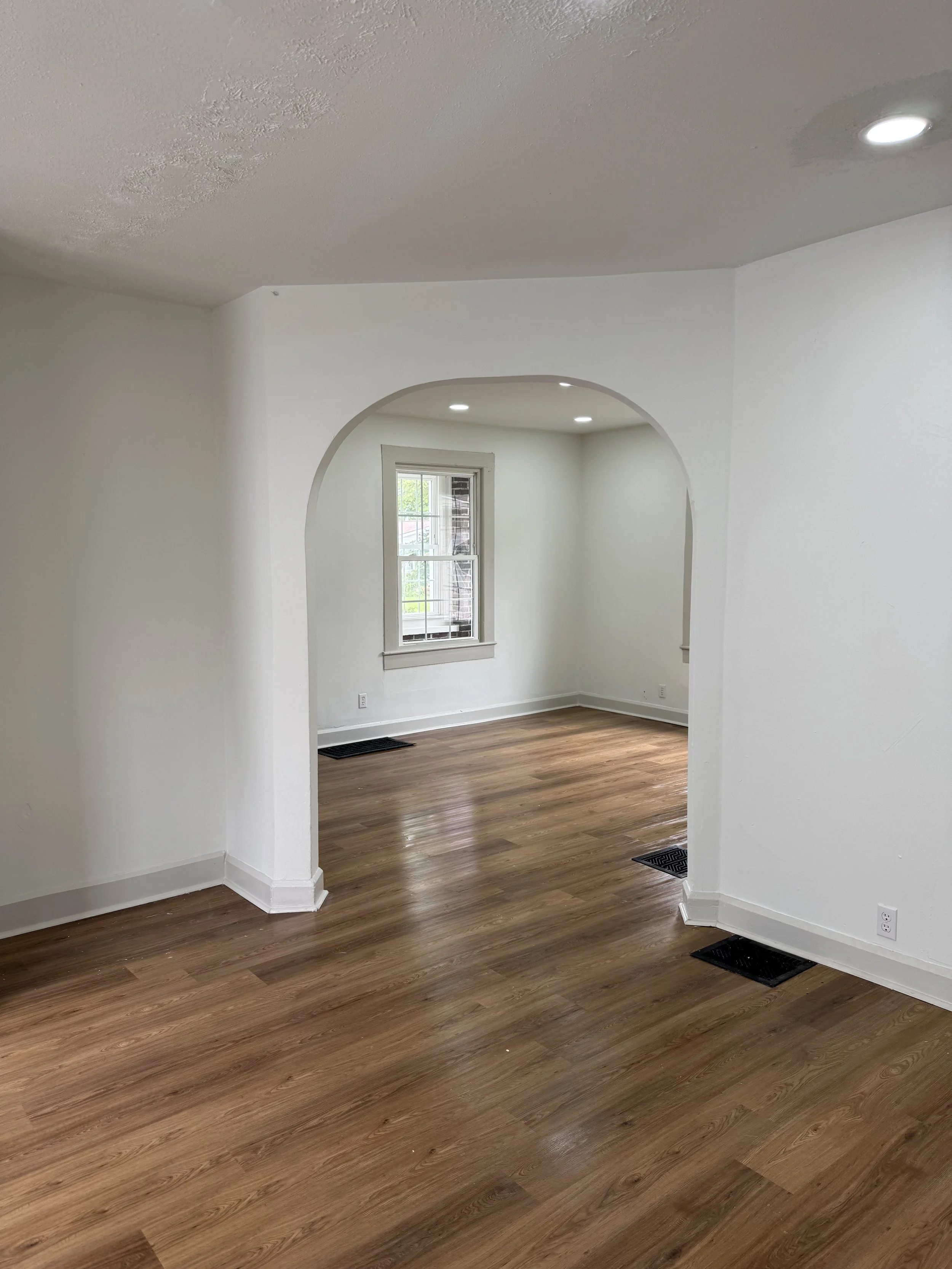 Empty room with hardwood floors, white walls, a window, and recessed lighting.