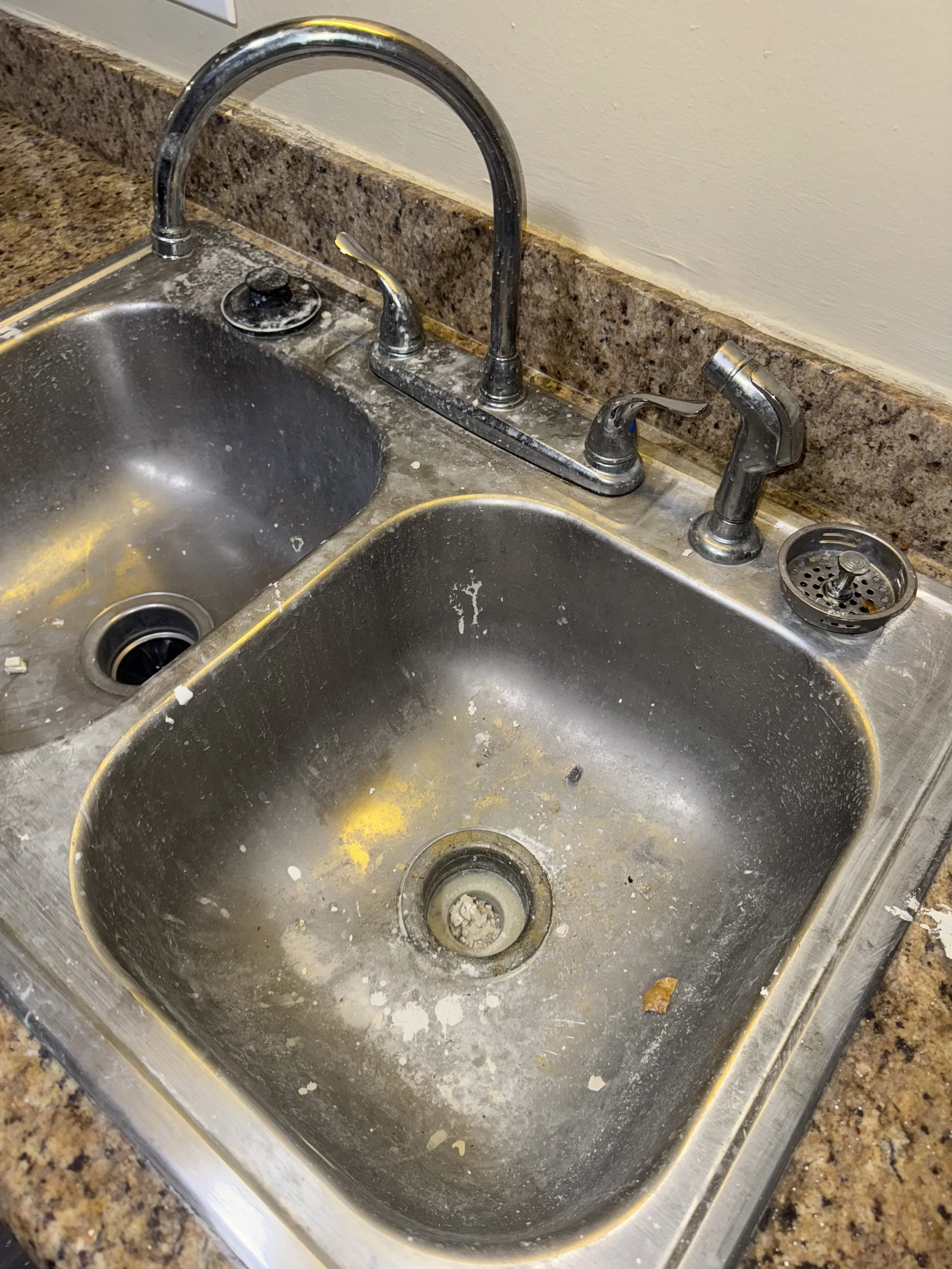 Dirty double kitchen sink with food debris, stains, and grime.