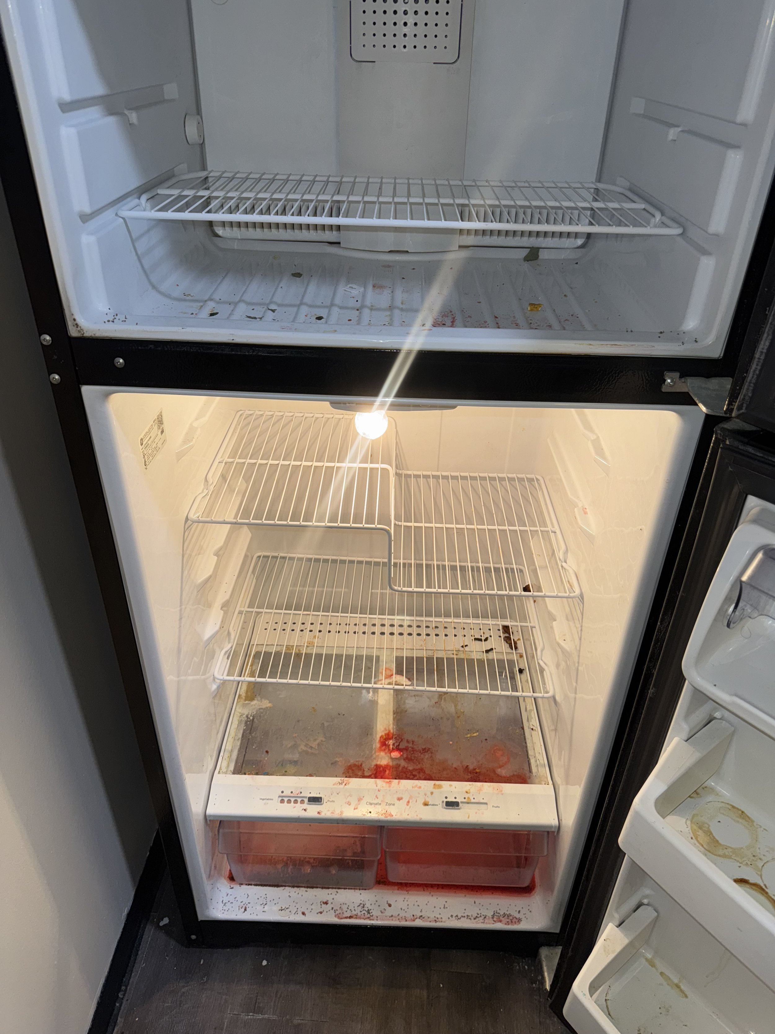 Empty refrigerator with some spilled food and stains on shelves and drawers.