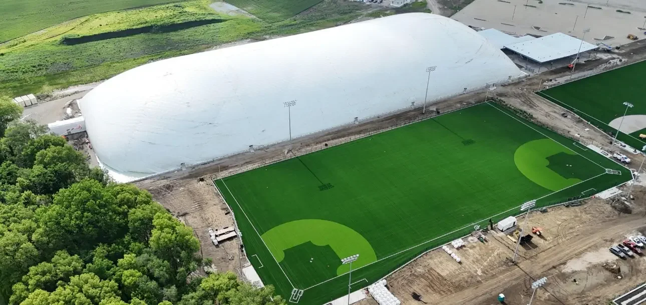 An aerial view of a sports complex with a baseball field under construction and a large white dome structure nearby.