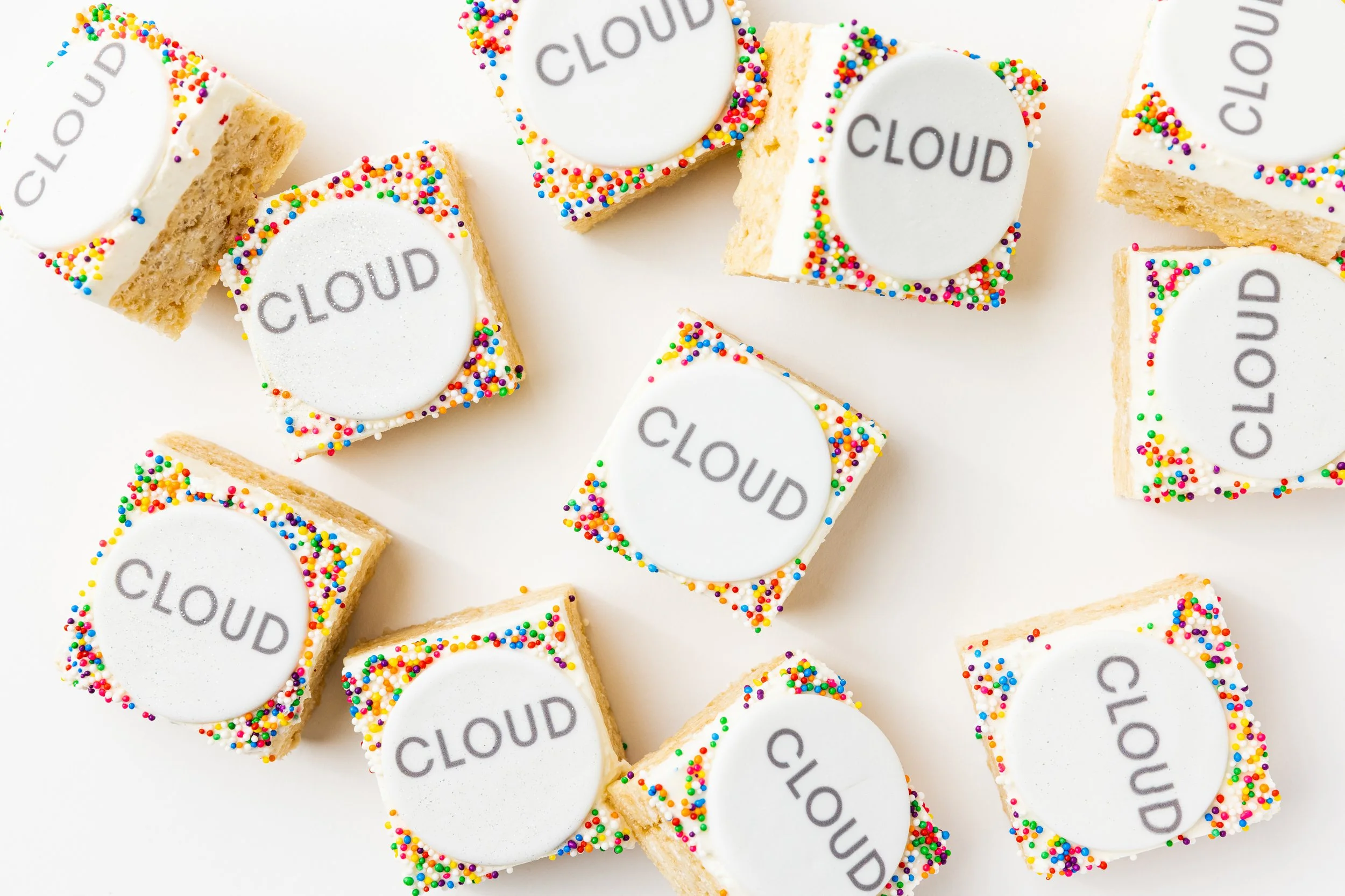 Square cookies with white icing, colorful sprinkles on the edges, and the word 'CLOUD' printed on round fondant toppers.