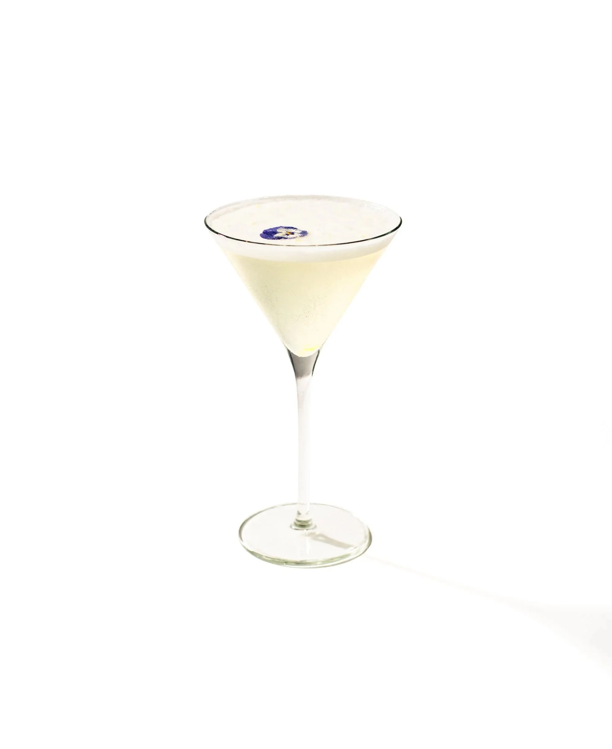 A martini glass with a white cocktail garnished with a blue flower.