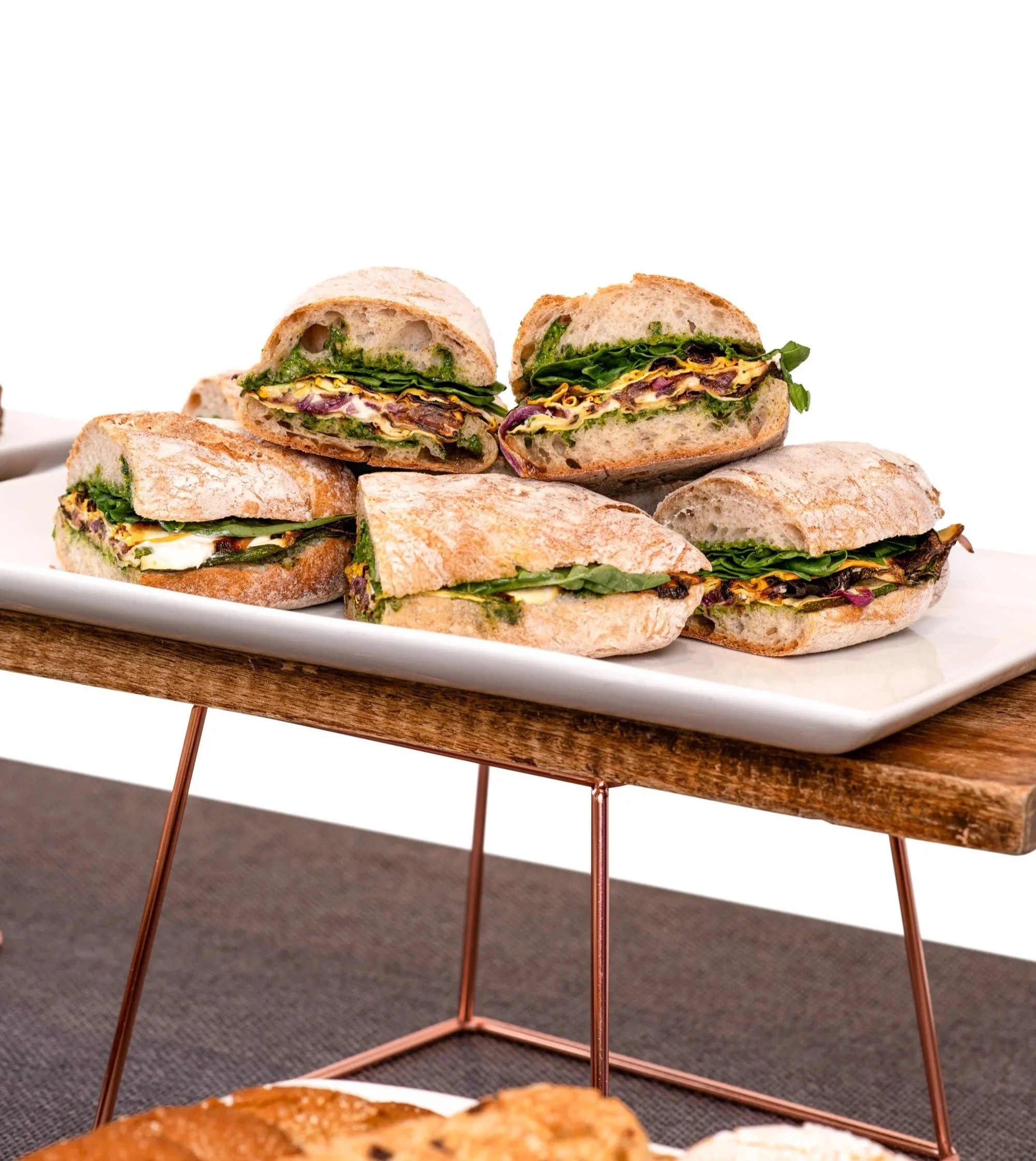 Assorted sandwiches with lettuce and vegetables on a white platter, placed on a wooden stand.