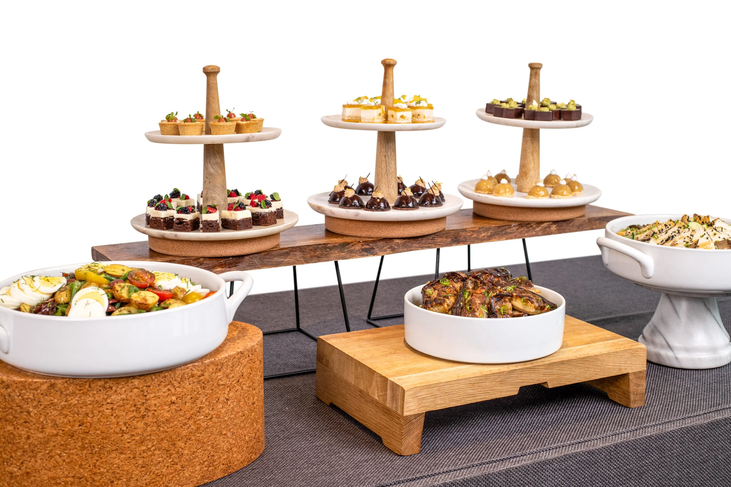 A variety of appetizers and desserts arranged on a table, including a large bowl of salad, a dish of chicken wings, and an assortment of small cakes and pastries on tiered serving stands.